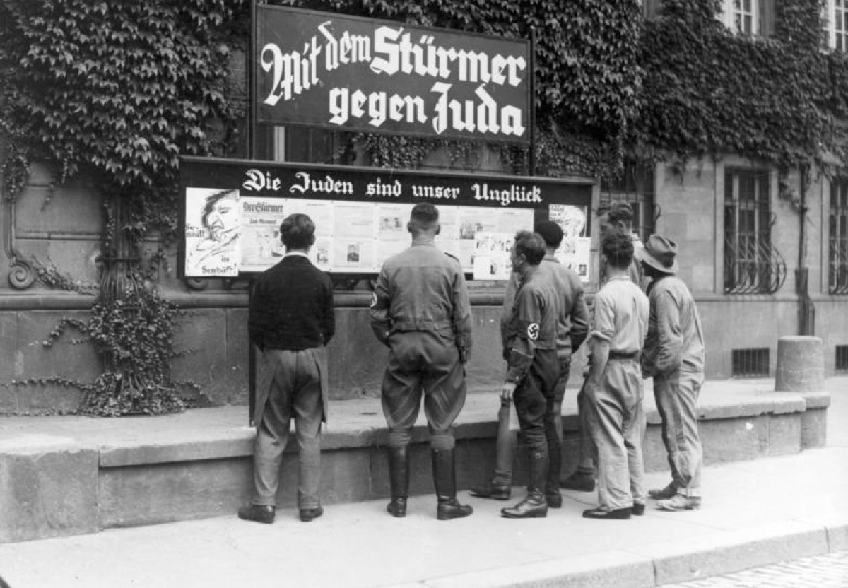 Men in Worms reading a Der Stürmer display case under a banner reading Mit dem Stürmer gegen Juda