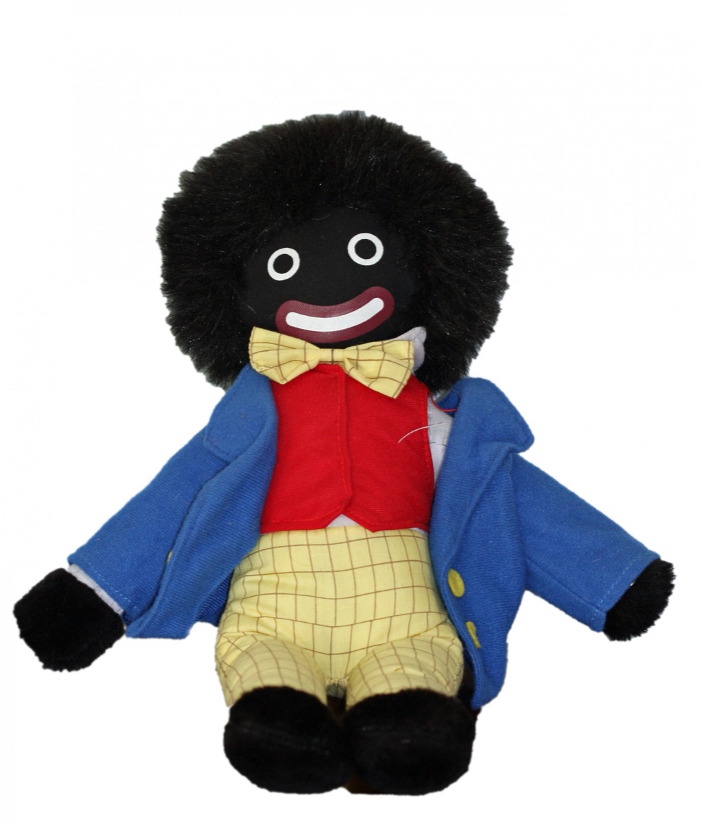 A golliwog soft toy with black fabric skin, a red waistcoat and a blue jacket