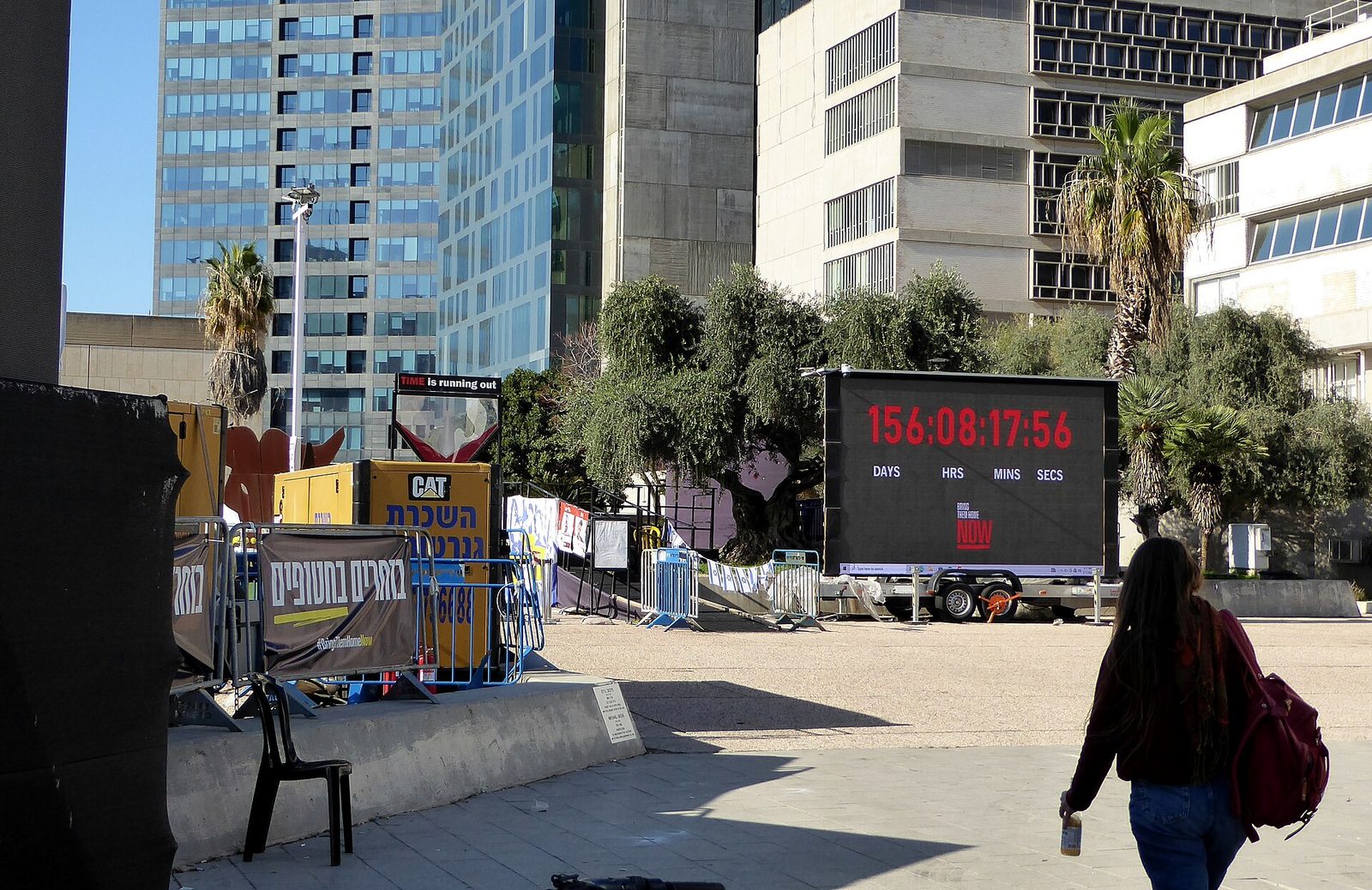 Large digital countdown screen in public square, barricades and signage, Tel Aviv