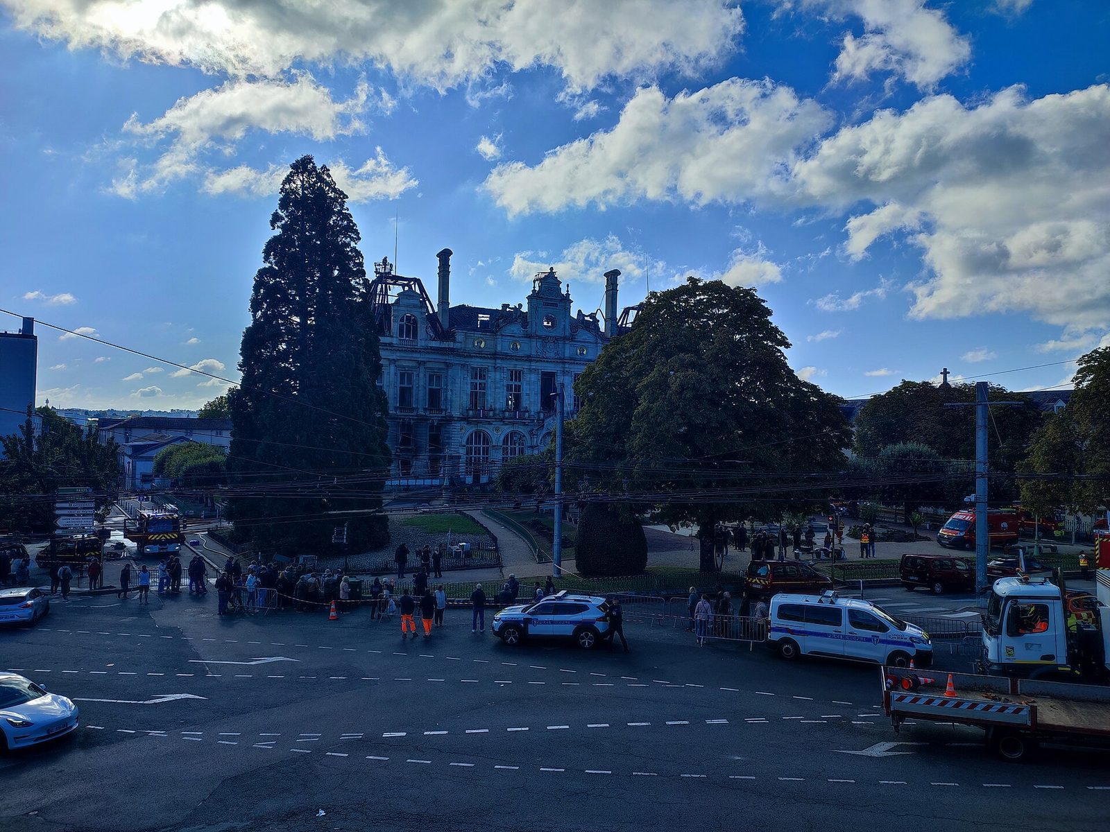 Ornate building with roof damage, emergency vehicles and onlookers