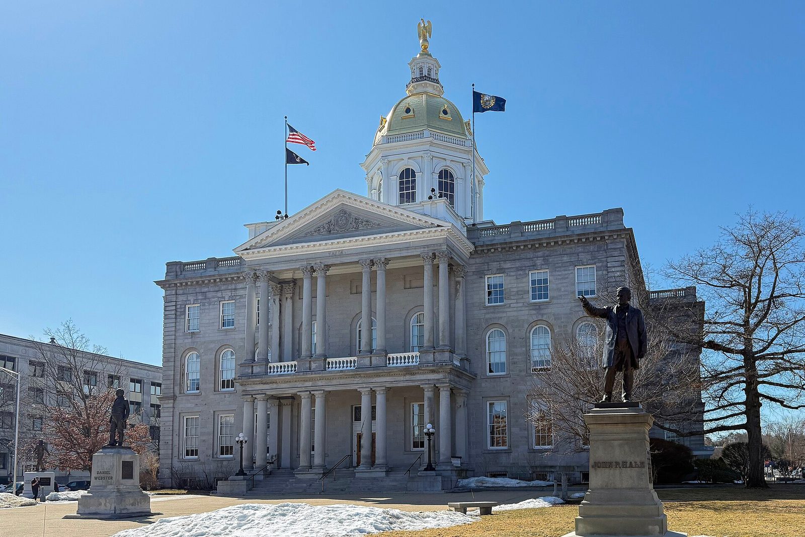 Stone government building with gold dome, columns, two statues, US flag, New Hampshire
