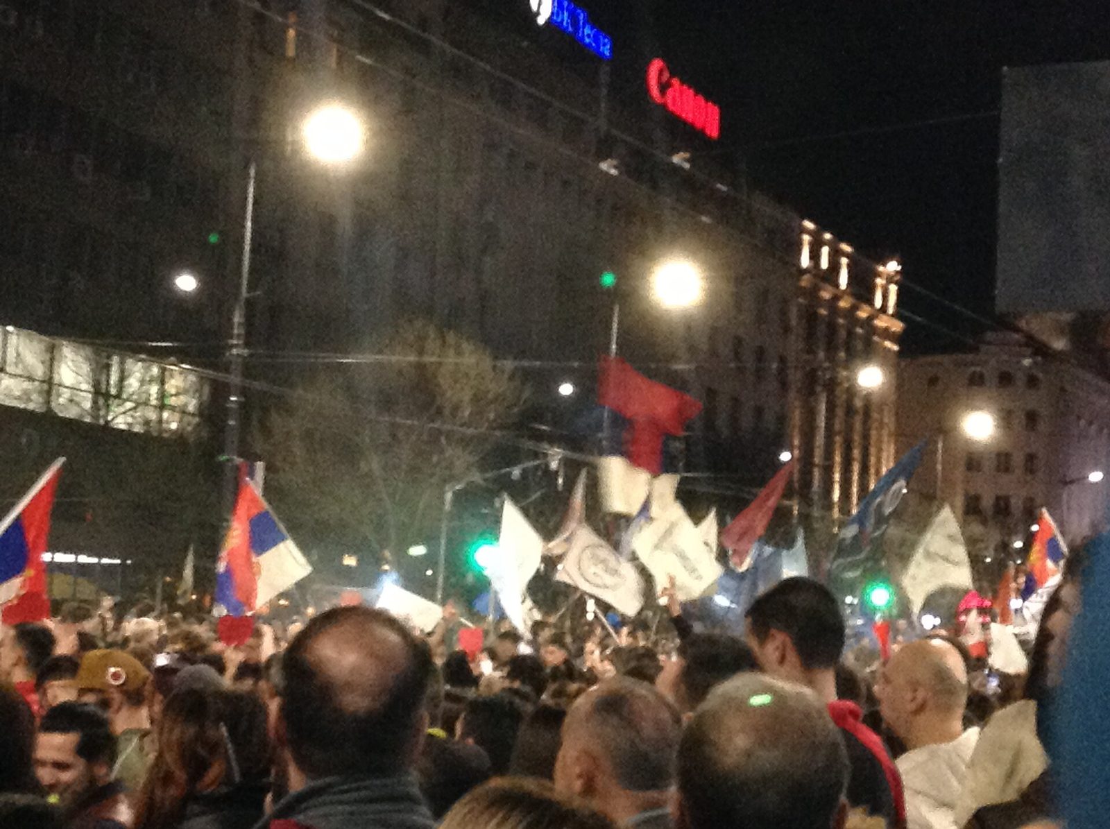 Large night-time crowd with flags and mobile phones raised, smoke in the