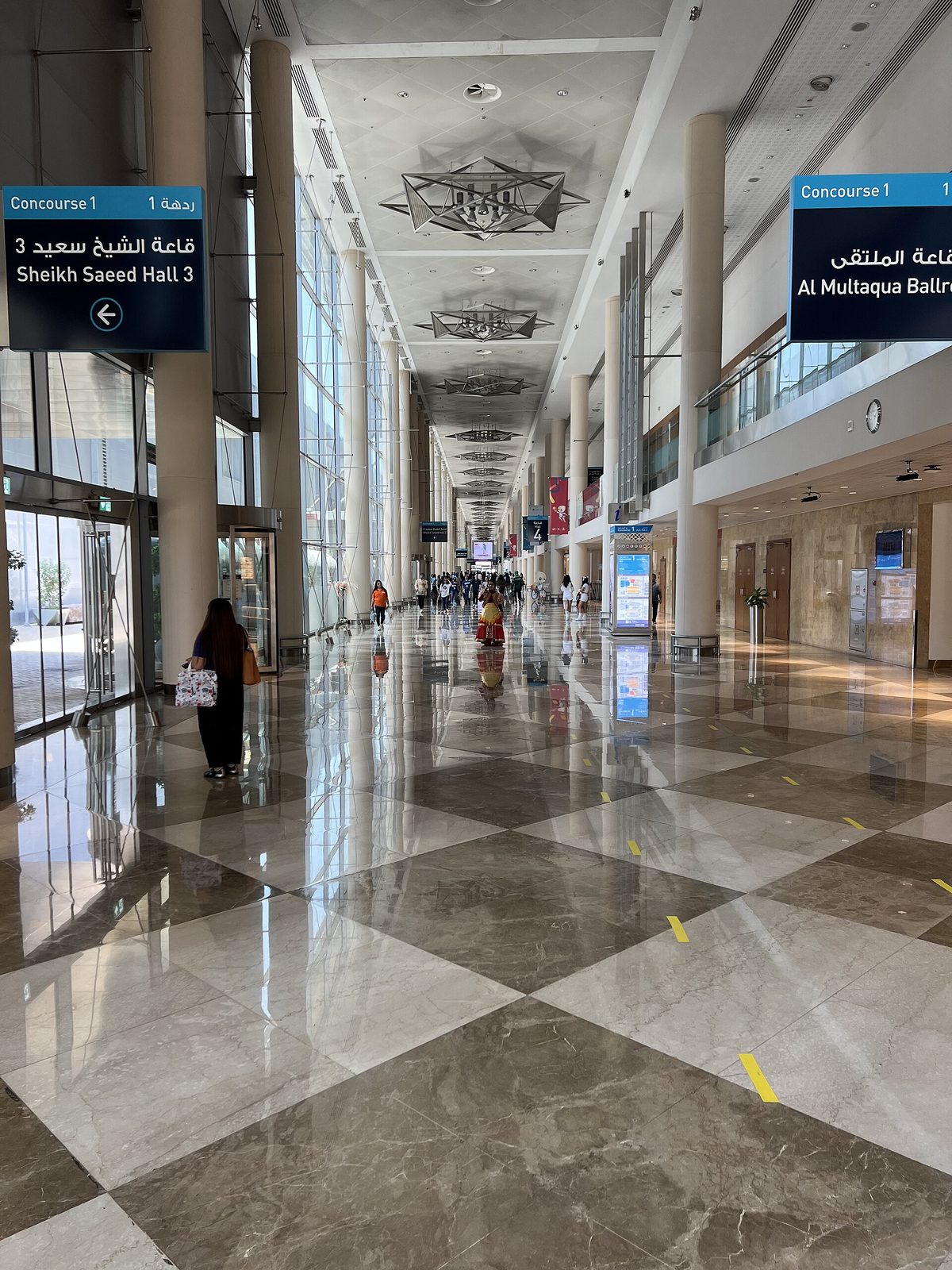 Long reflective concourse inside exhibition centre, signage for halls, scattered people, Dubai World Trade Centre