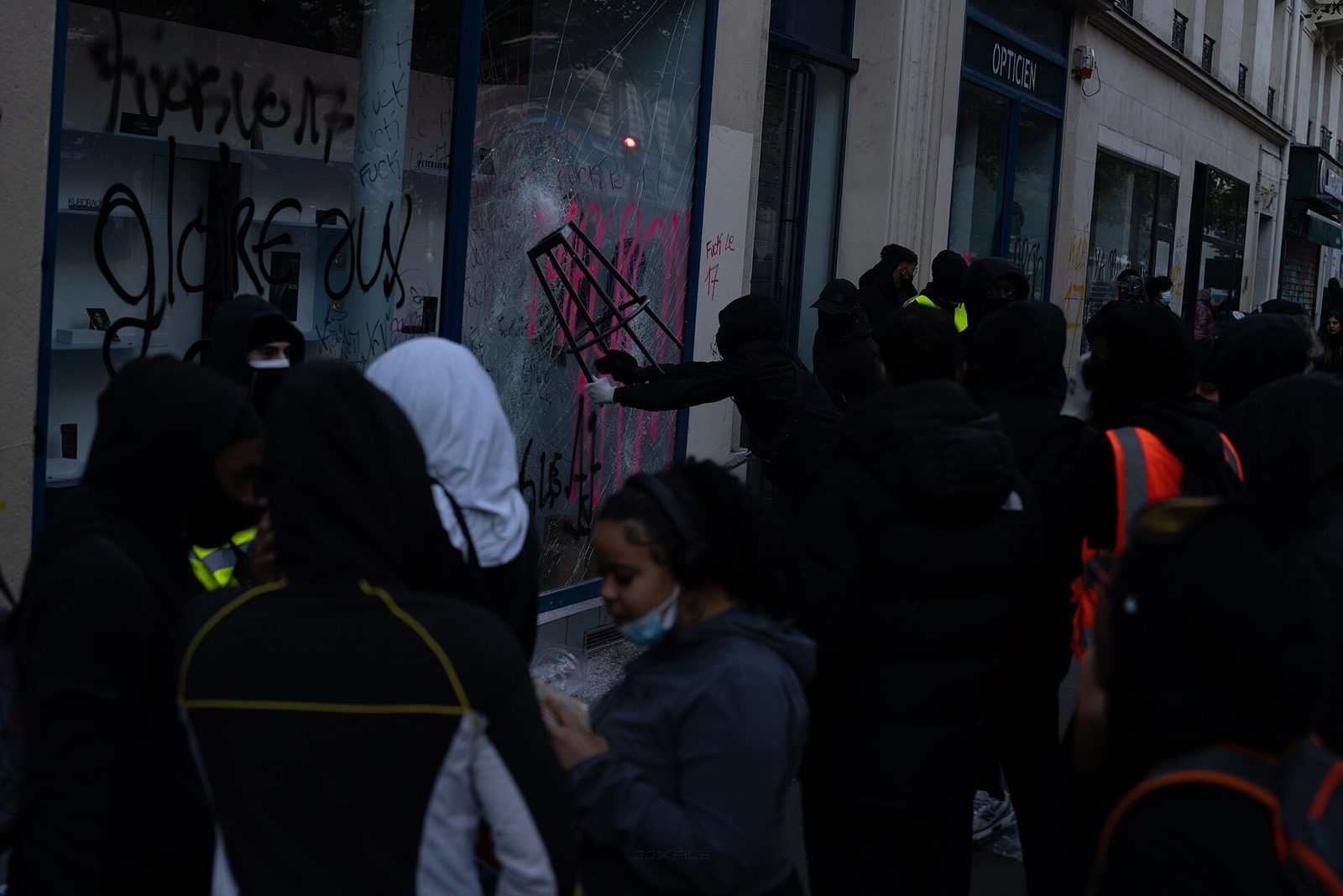 people gathered around smashed, graffitied shopfront, broken glass, France