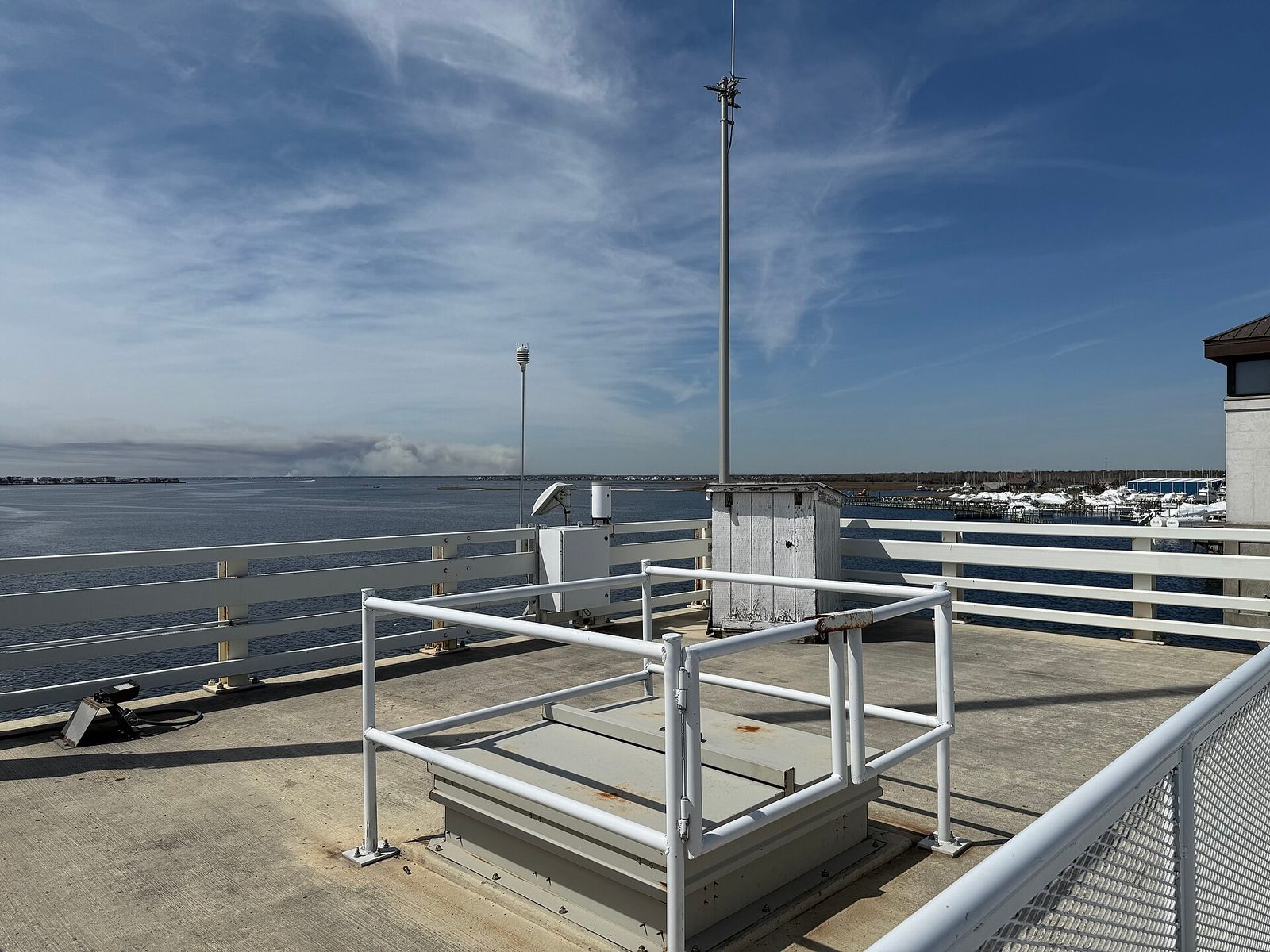 Weather instruments and boxes on bridge overlooking bay, smoke plume