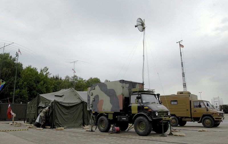 Camouflaged military vehicles, tents, and tall satellite antennas in compound