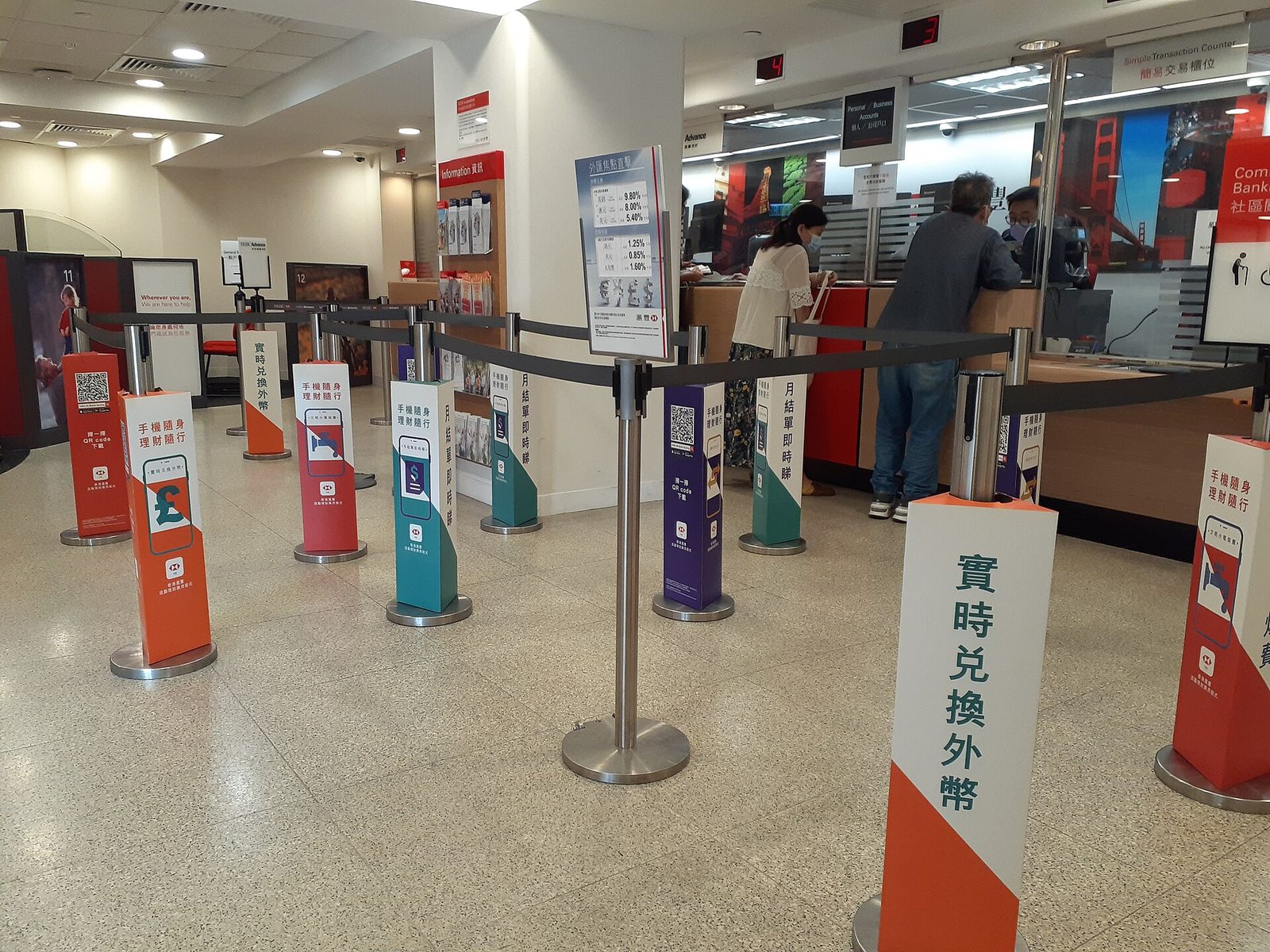 Bank interior with queue posts, customers at service counters, promotional signage., Hong Kong