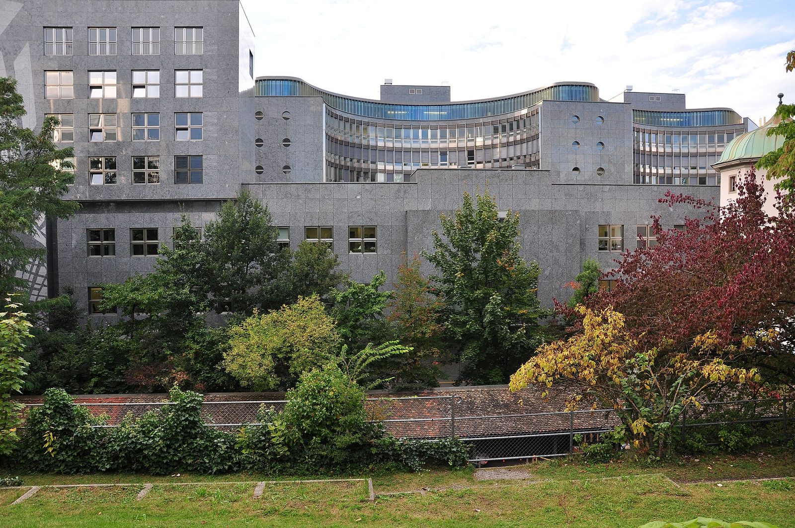 curved grey stock exchange building, trees and grassy foreground, Switzerland