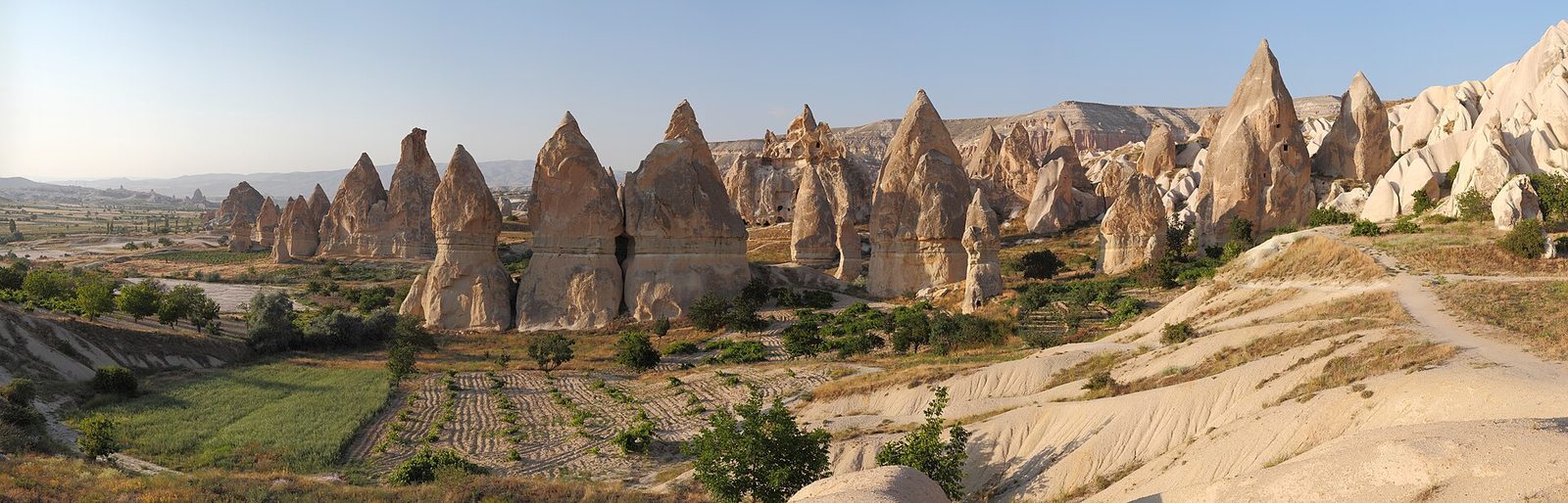 Line of tall fairy chimneys across a cultivated valley, clear sky