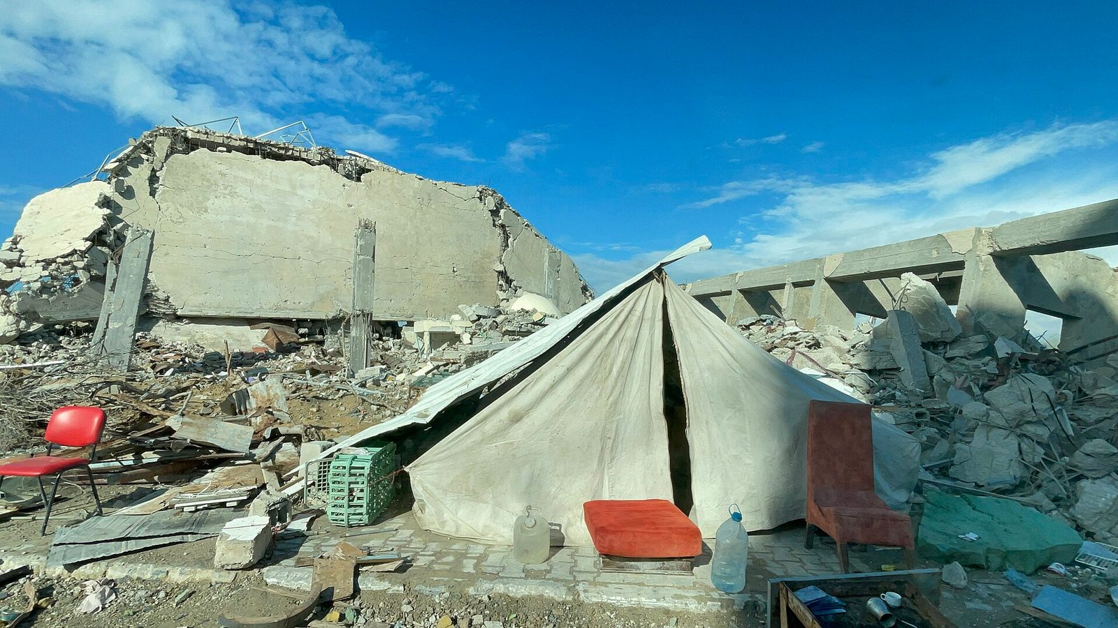 small tent pitched among concrete rubble, chairs and debris in foreground