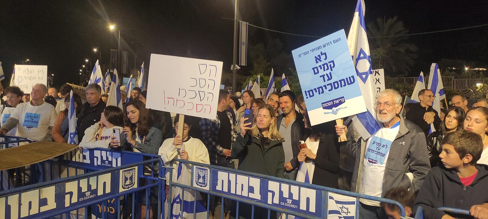 People holding placards and Israeli flags behind barricades, night, Jerusalem