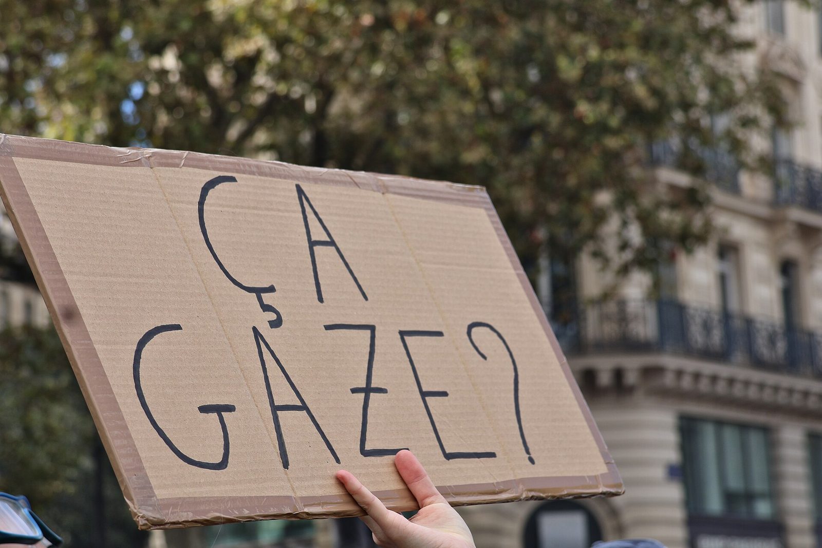 Large cardboard sign reading 'CA GAZE?' held above a crowd, Place de la République