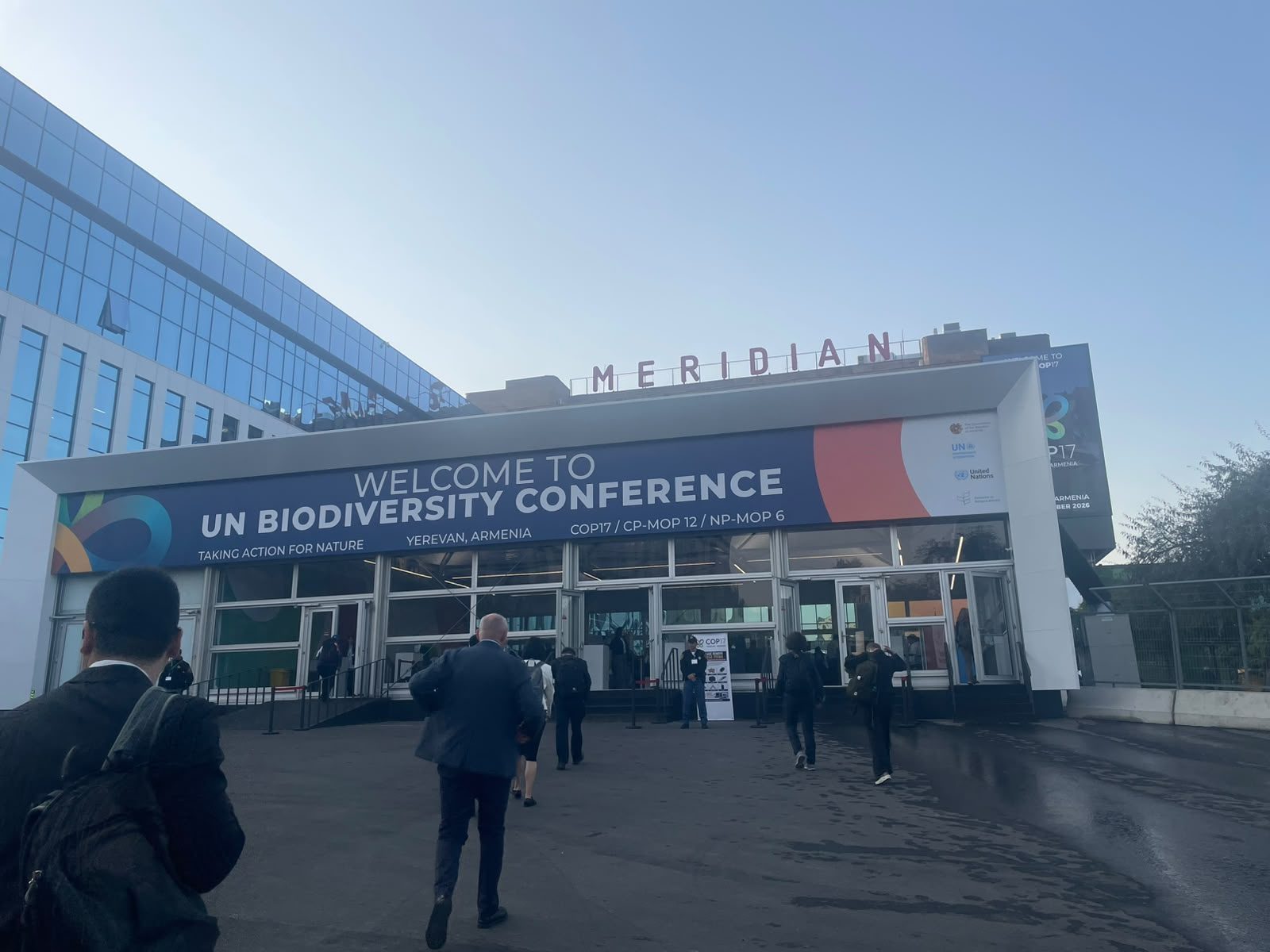 Main accreditation entrance with COP17 banner, delegates walking towards doors, Yerevan