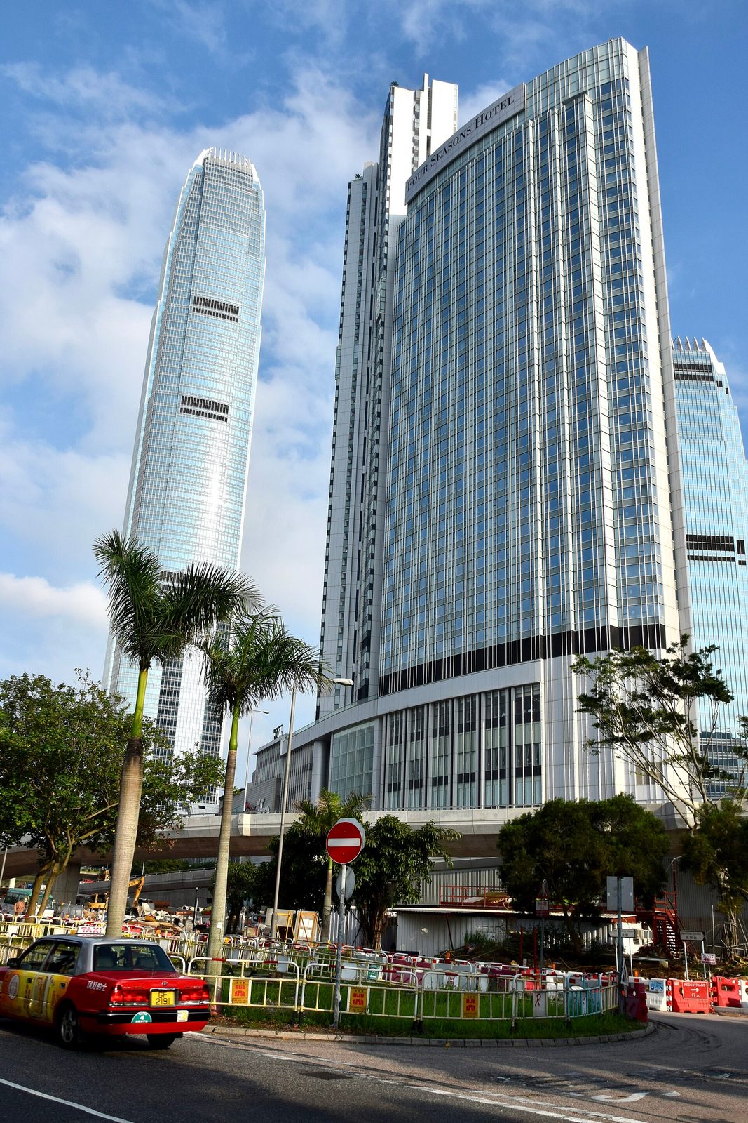 Glass-fronted skyscrapers and palm trees, red taxi in foreground, Hong Kong