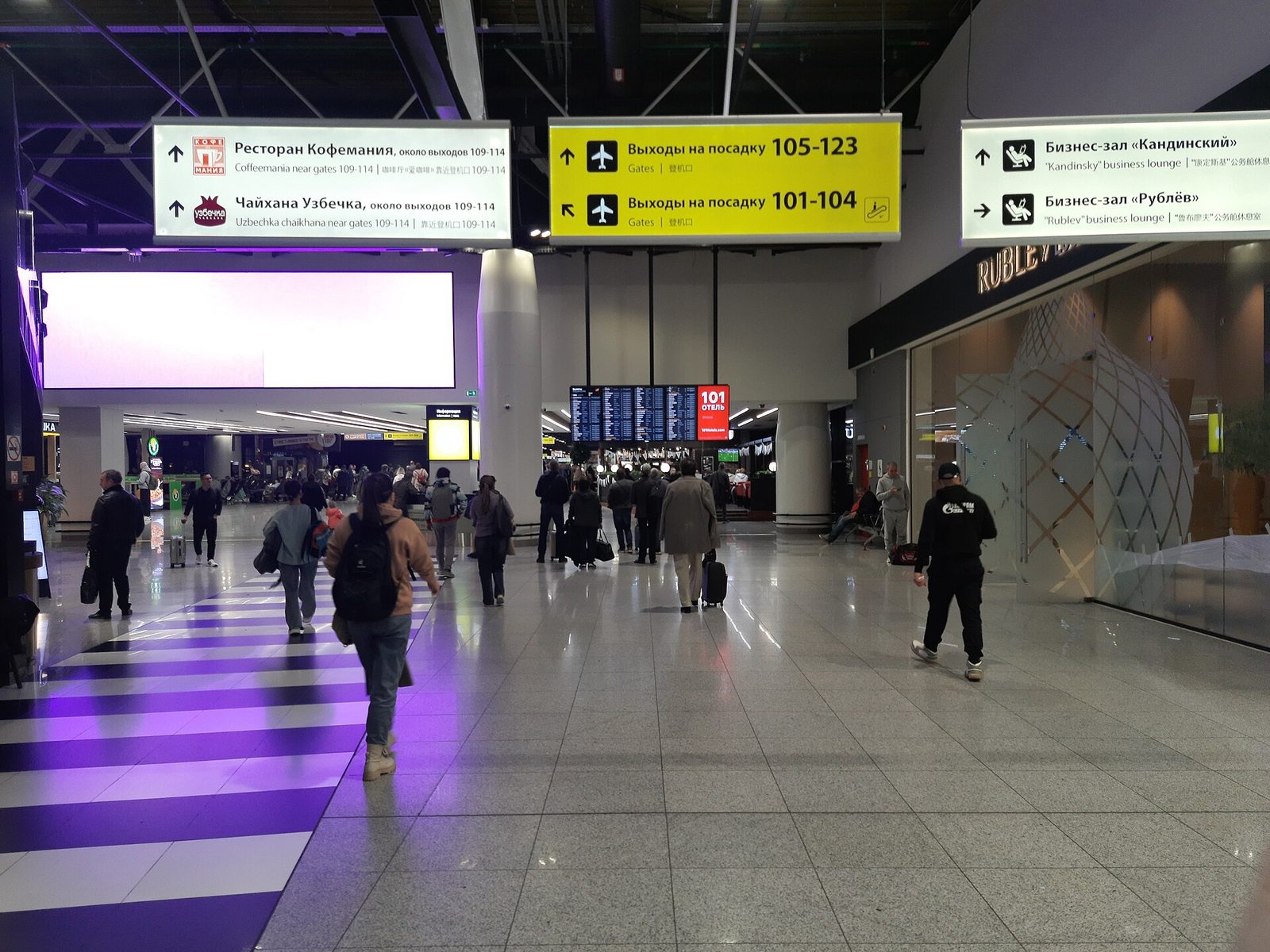 wide airport concourse, passengers walk towards gates under overhead signs