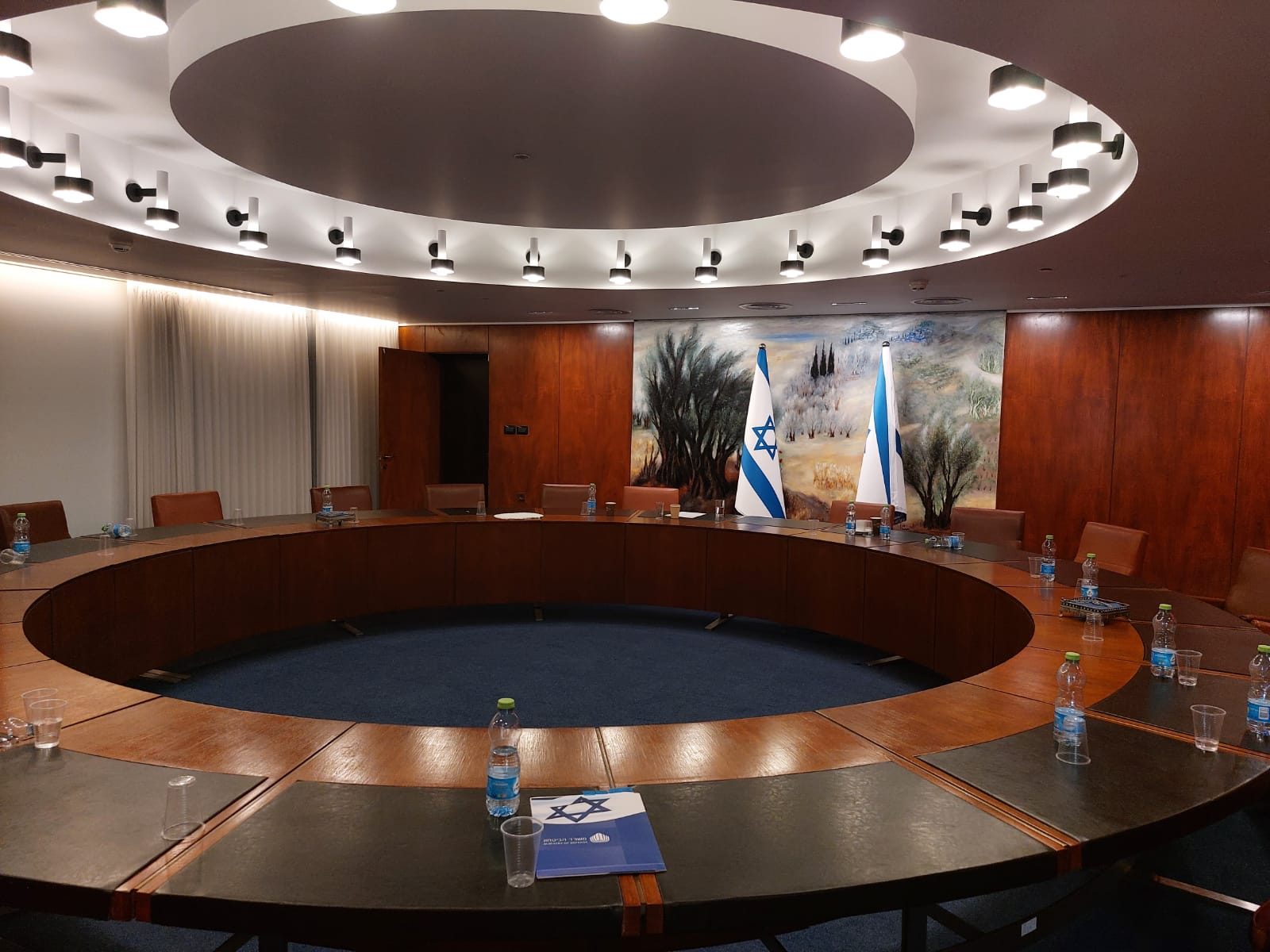 Round wooden conference table, chairs, two flags and mural on the wall