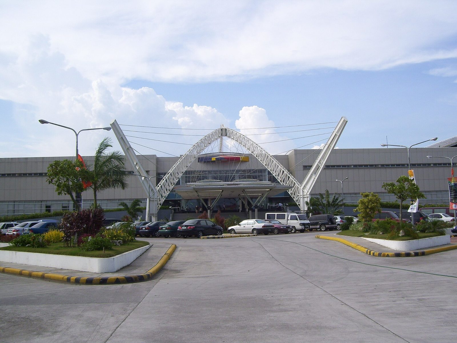 Convention centre entrance with arched steel canopy, parked cars, cloudy sky., Cebu