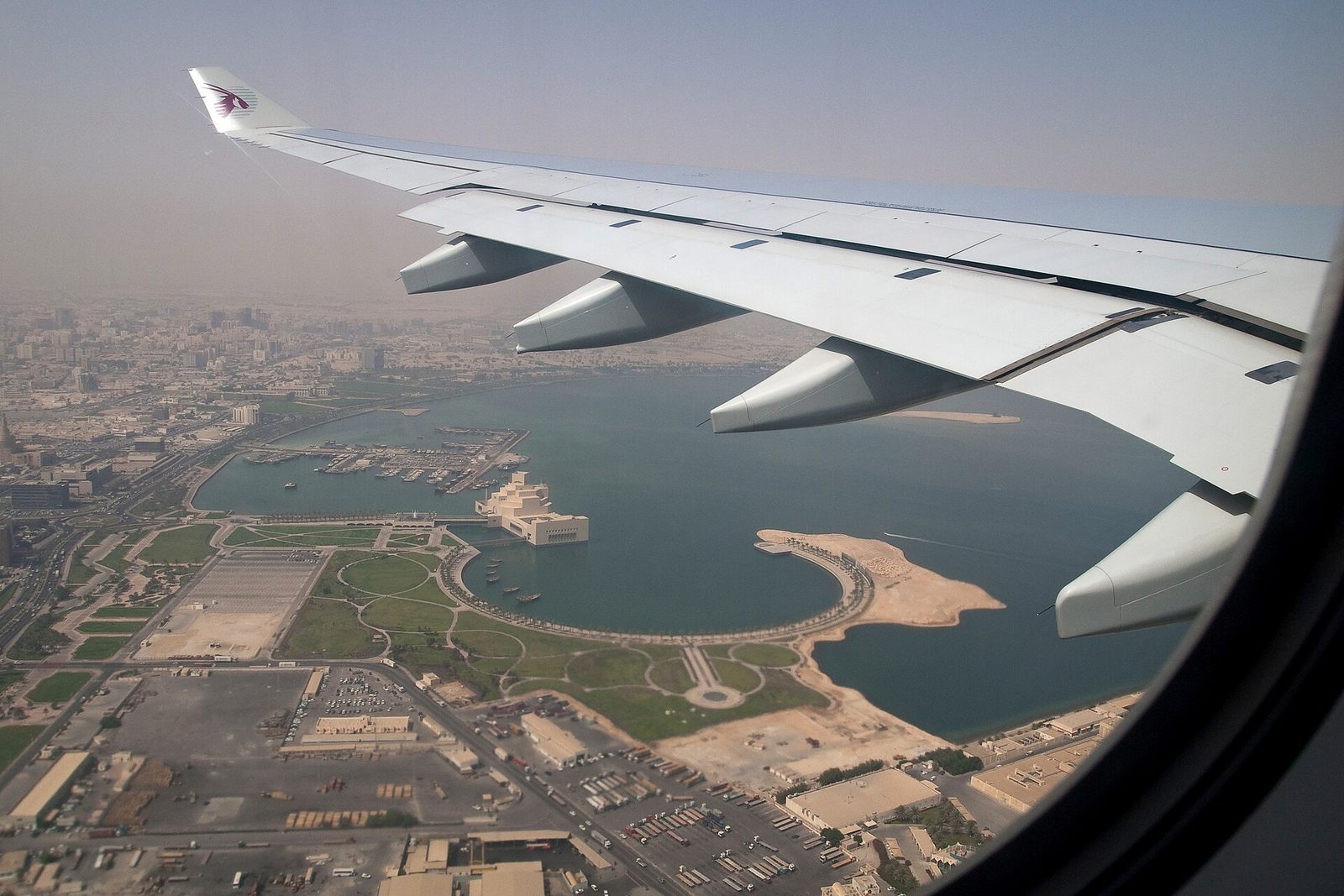 Airplane wing over Doha bay, waterfront and city visible below