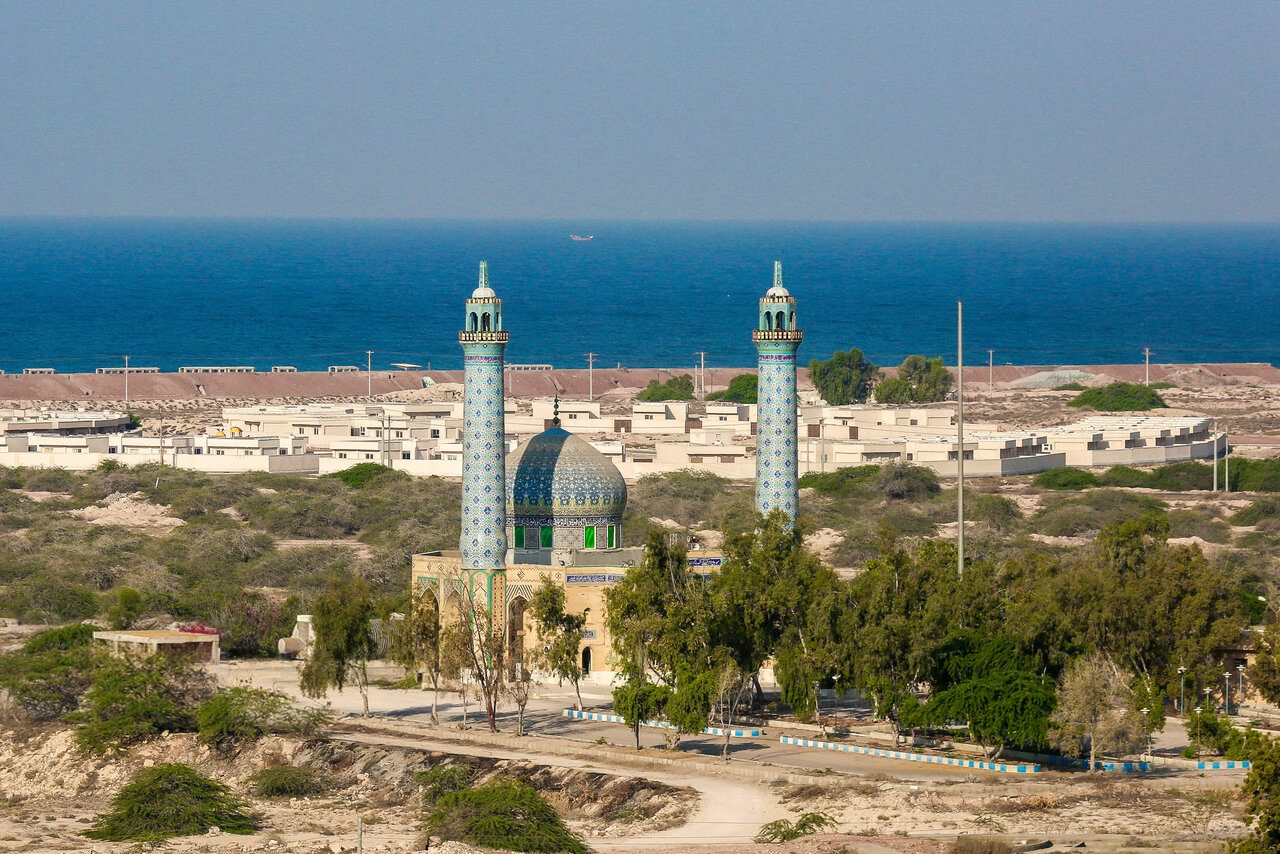 mosque with two tiled minarets, low buildings, sea on horizon