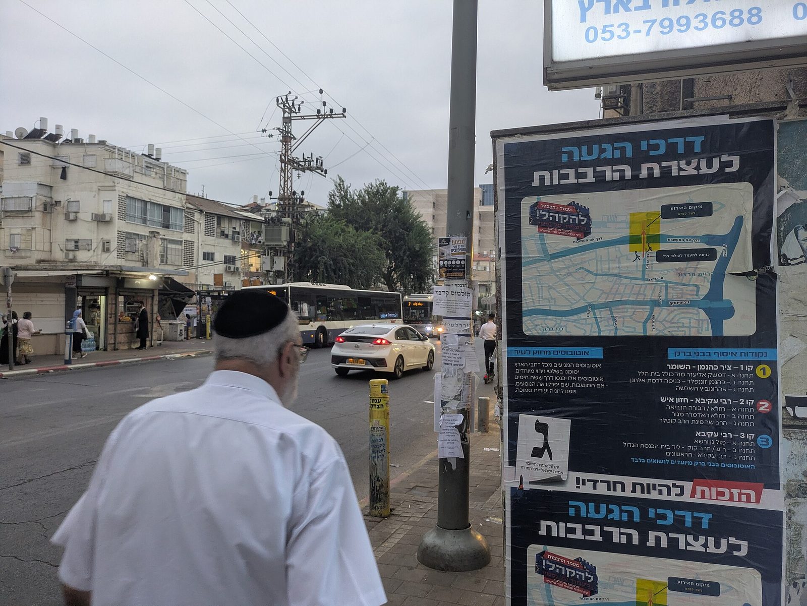 Man walking past bus, large map poster with Hebrew election information