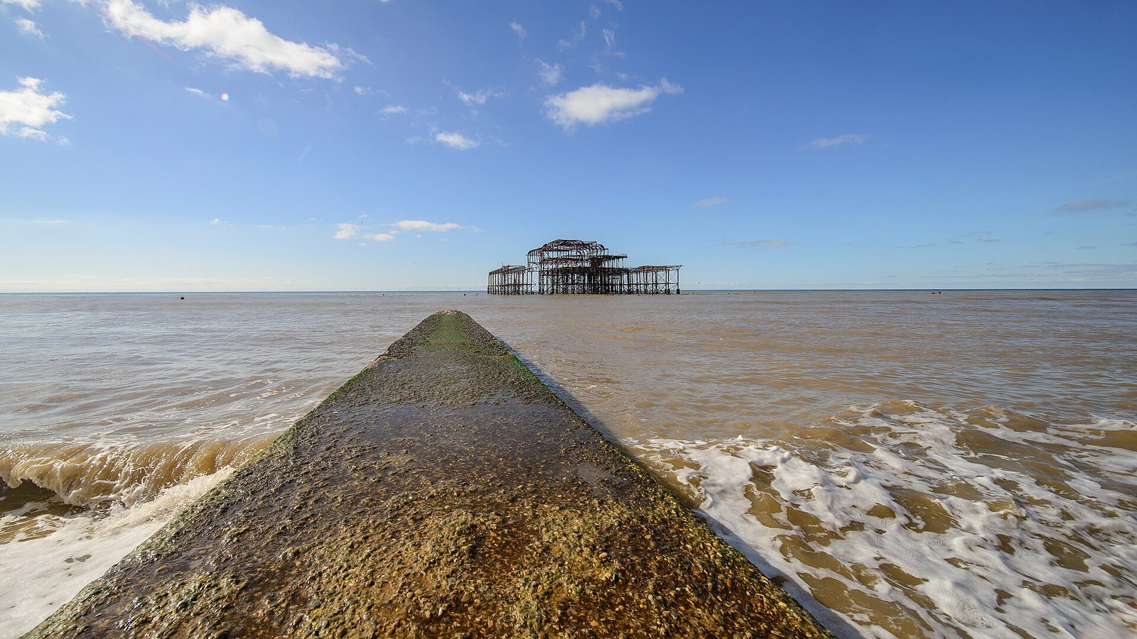 concrete groyne leading out to a skeletal pier, sea washing over it, Brighton