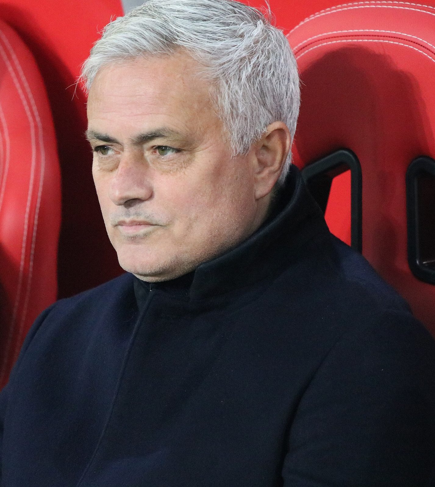Close side-profile of a man sat on a stadium bench, serious expression