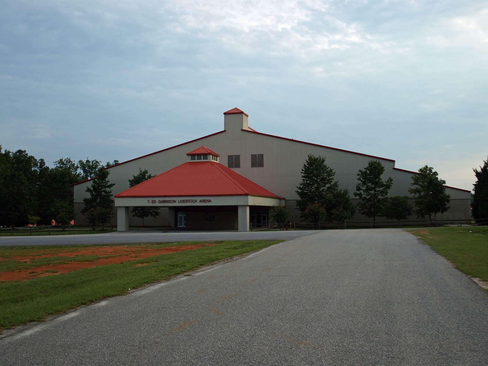 Large arena building with red-roofed entrance, paved driveway, surrounding trees, South Carolina