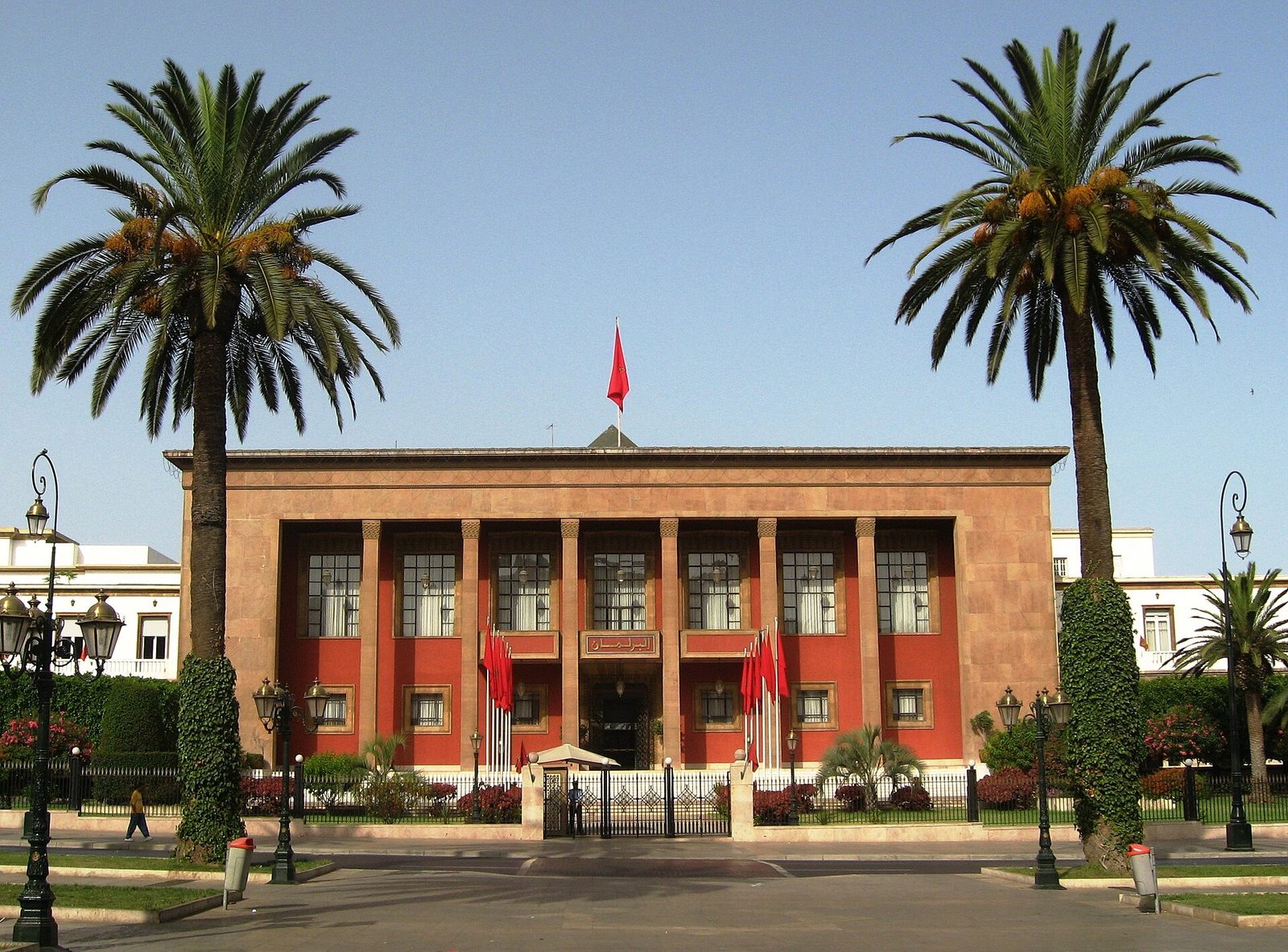 Parliament building façade, red flag, palm trees, gated forecourt, Rabat