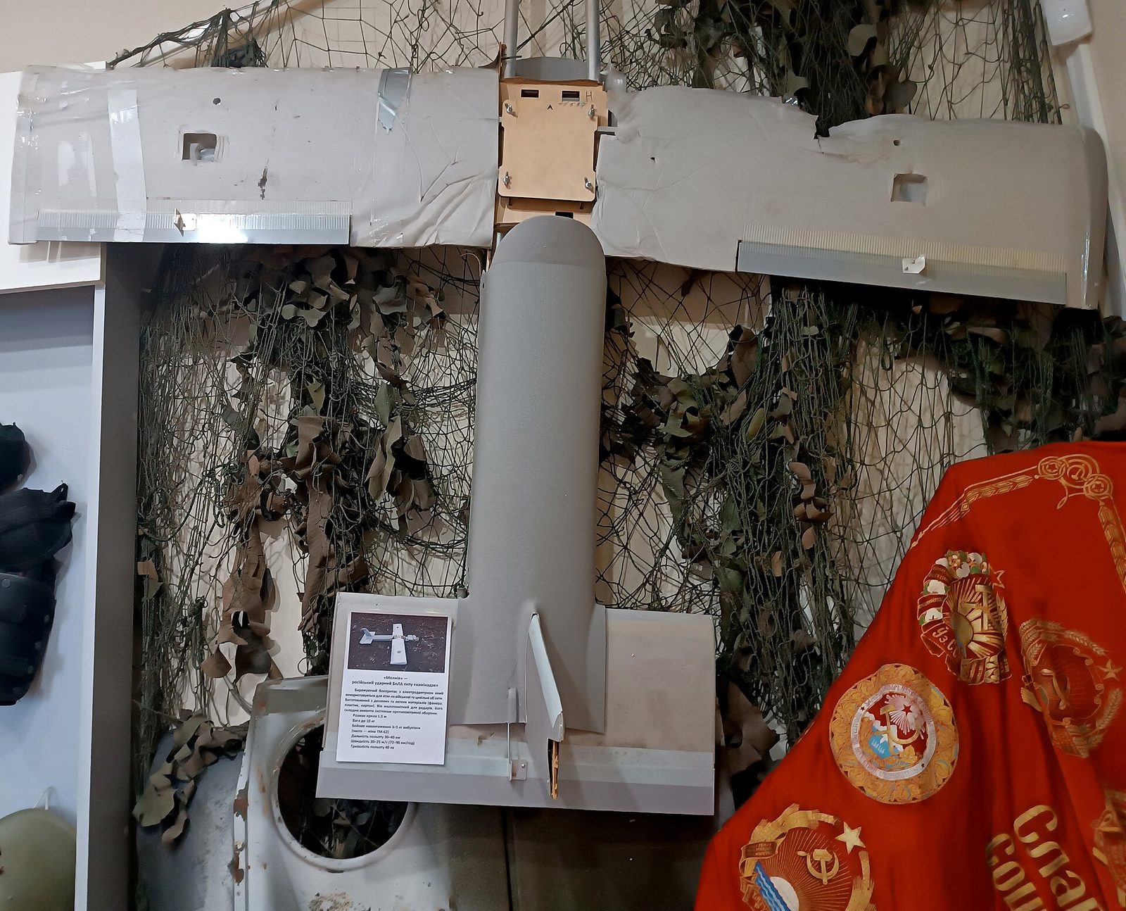 Wreckage of a small unmanned drone displayed against camouflage netting