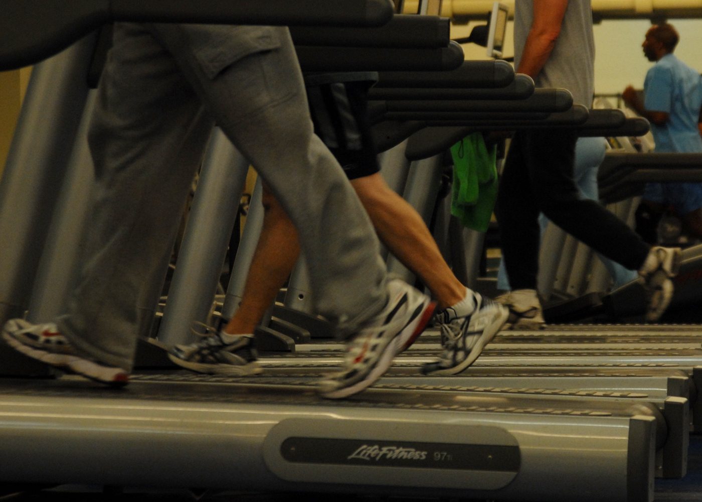 row of treadmills with several people running, legs visible