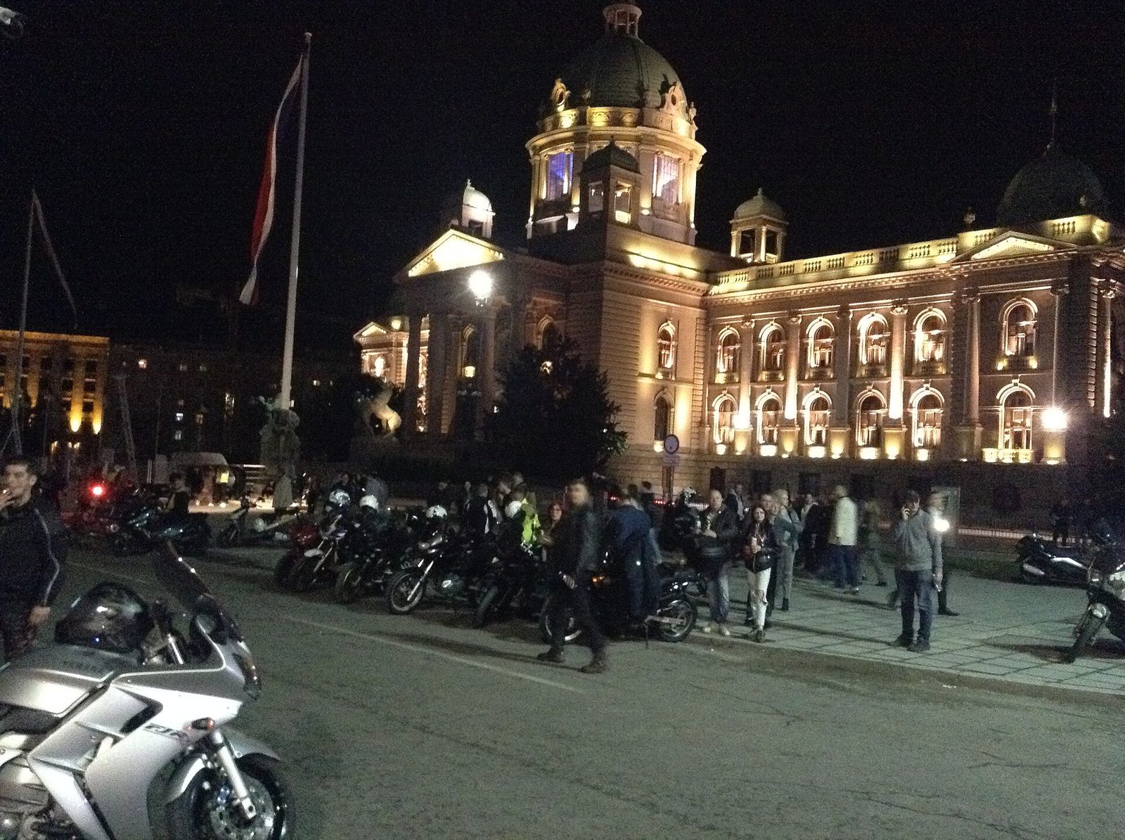 Crowd and bikers in front of the National Assembly building at night.