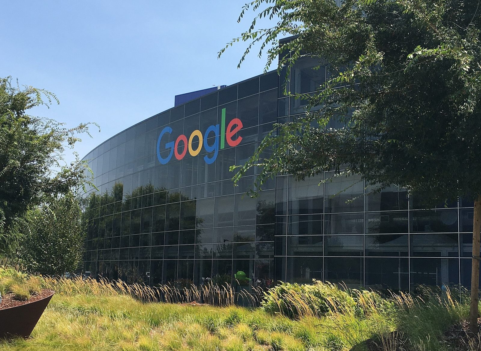 Curved glass office facade with large Google logo, grasses in foreground