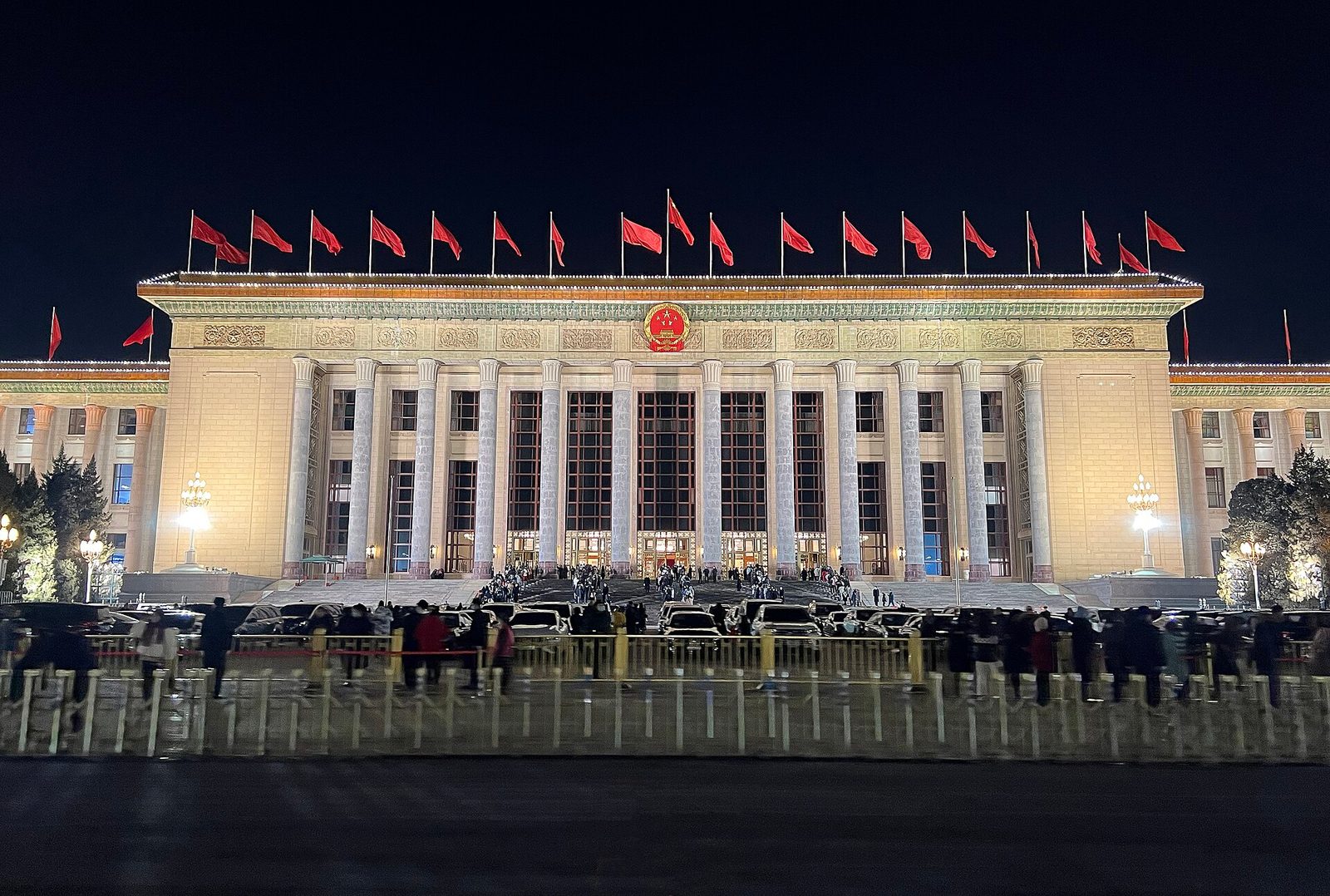 government building brightly lit at night, flags on roof, crowds, Beijing