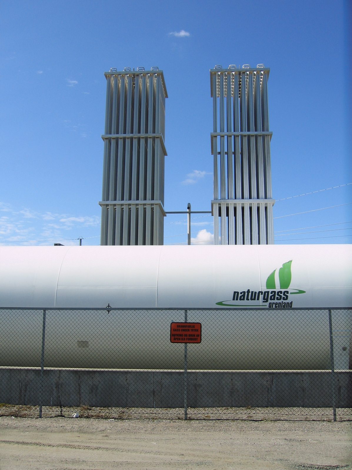 Large LNG storage tank, vertical evaporator columns, fence in foreground