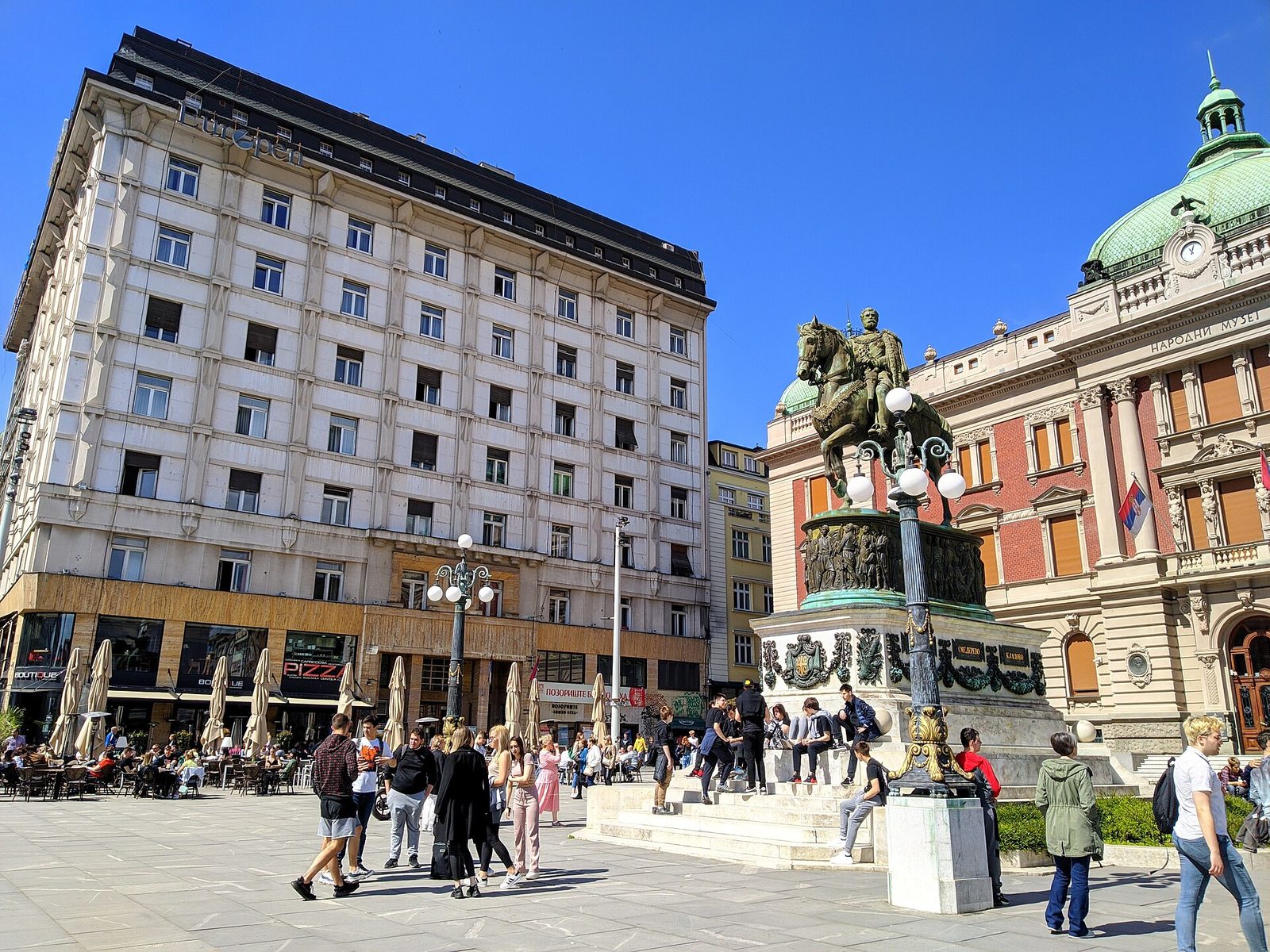 Crowd around an equestrian statue in a busy city square, sunny day, Belgrade