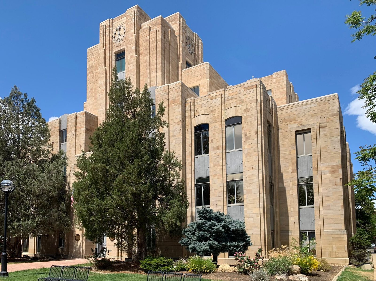 Art Deco courthouse exterior, sandstone facade, trees and benches on lawn, Boulder