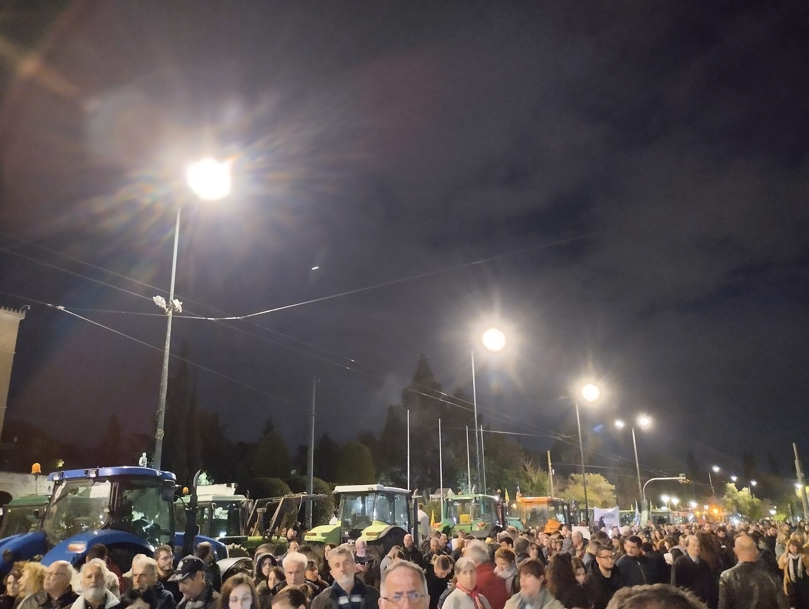 Crowd and tractors parked along a lit city square at night, Athens