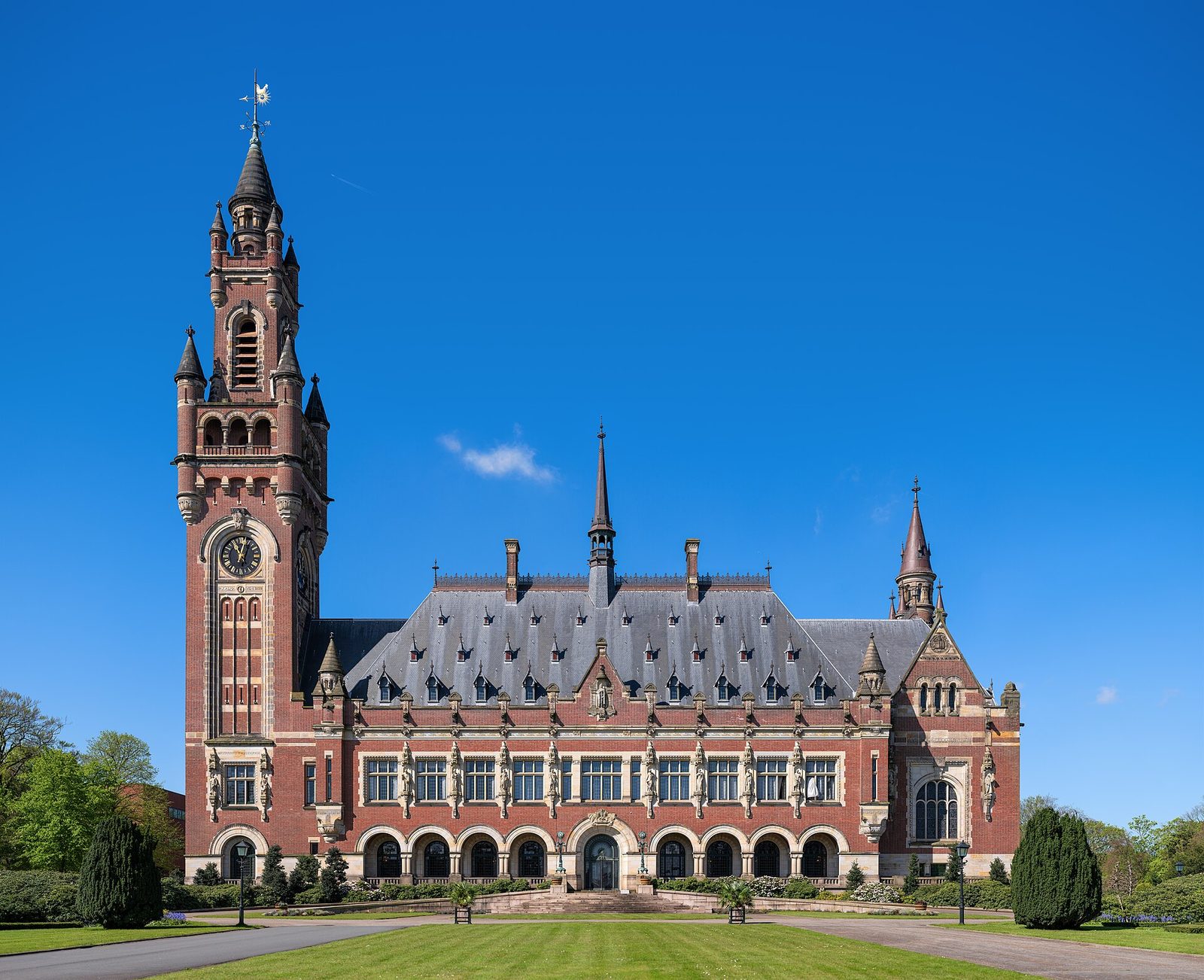 ornate red-brick palace facade with tall clock tower and lawn, The Hague