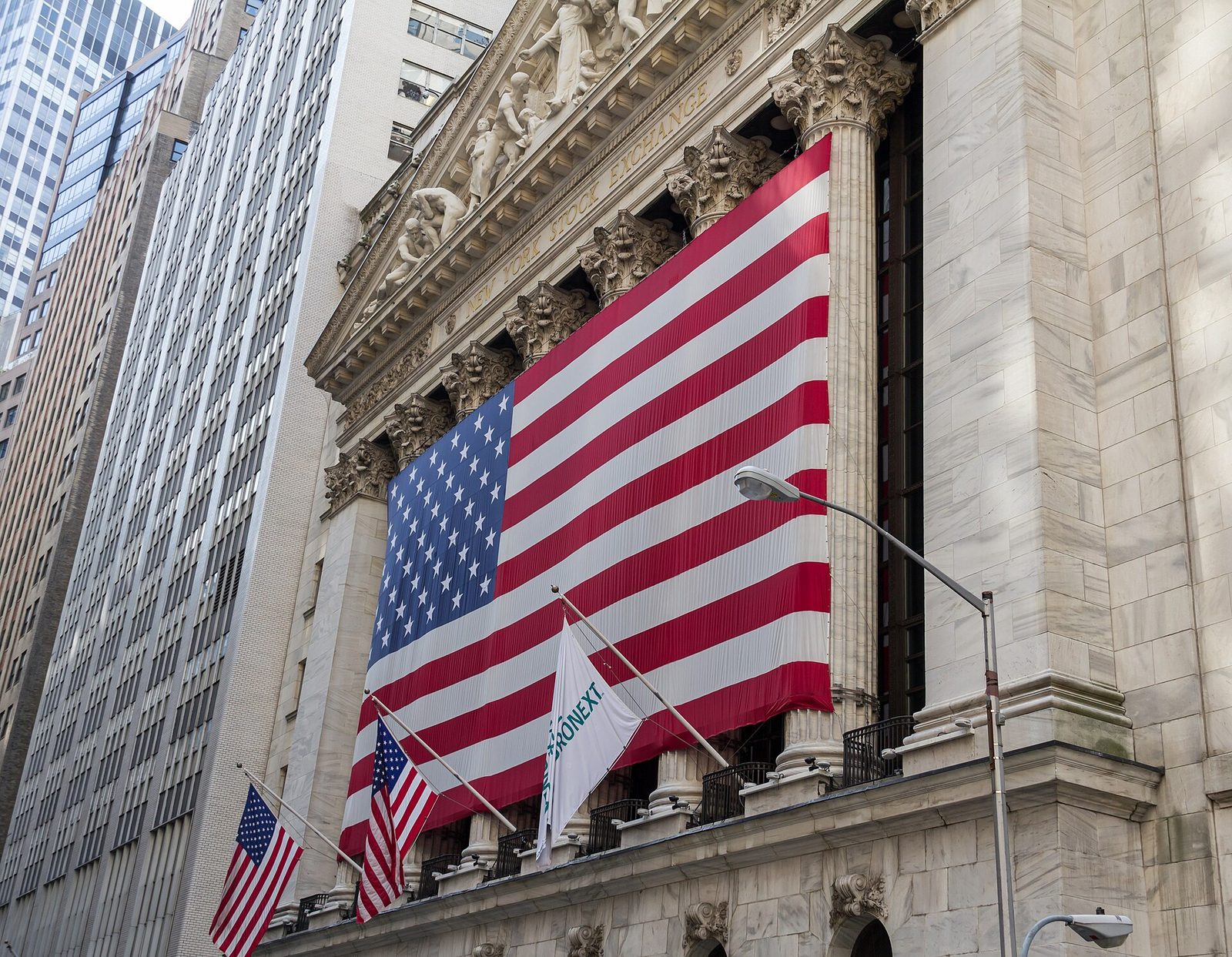 Large US flag draped over stock exchange facade, columns visible, United States