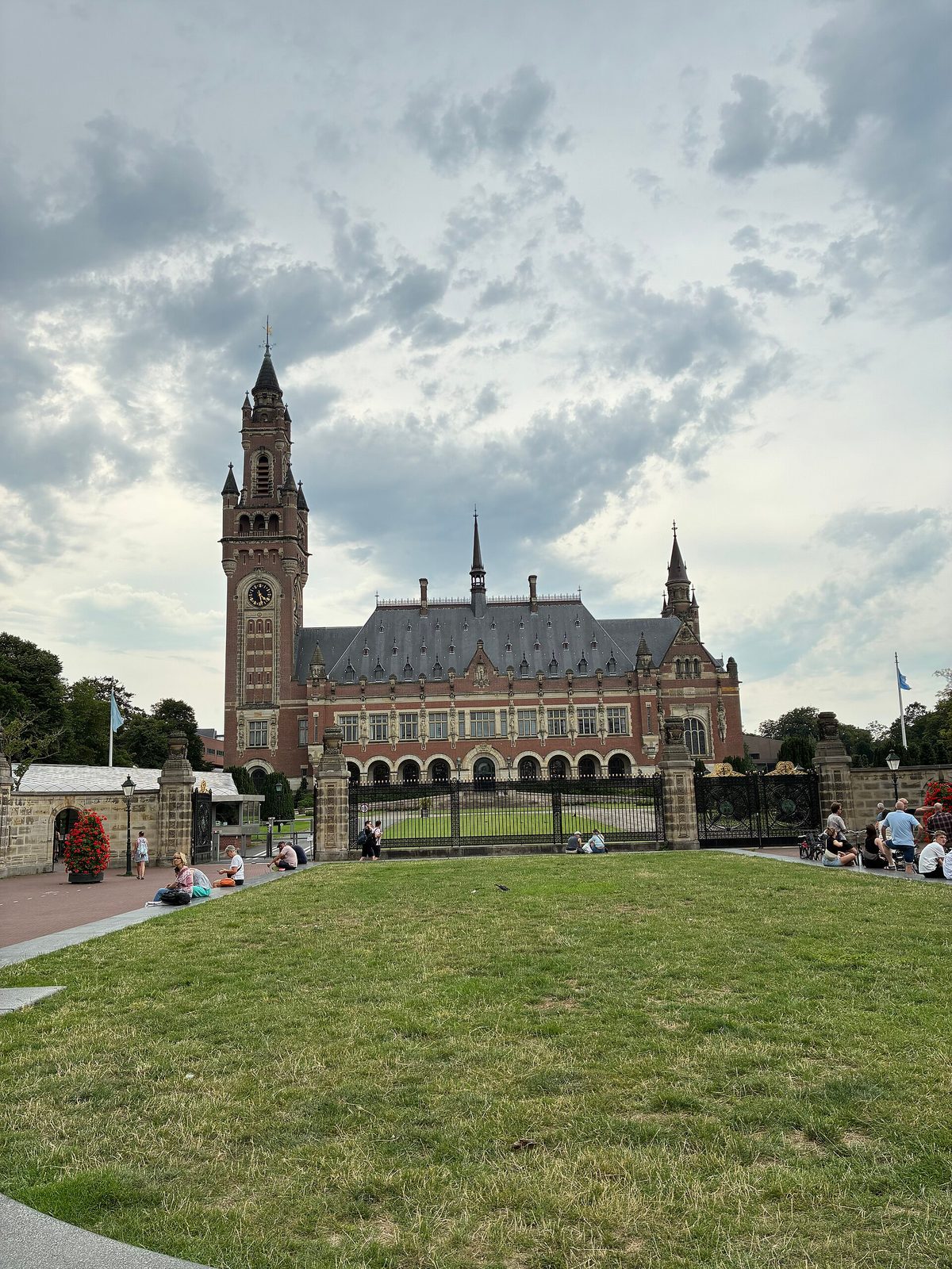 front view of red-brick palace, gated entrance, people on lawn, The Hague