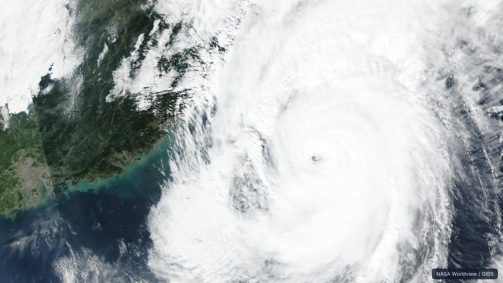 Large swirling cyclone cloud over ocean, coastal land at left, Taiwan