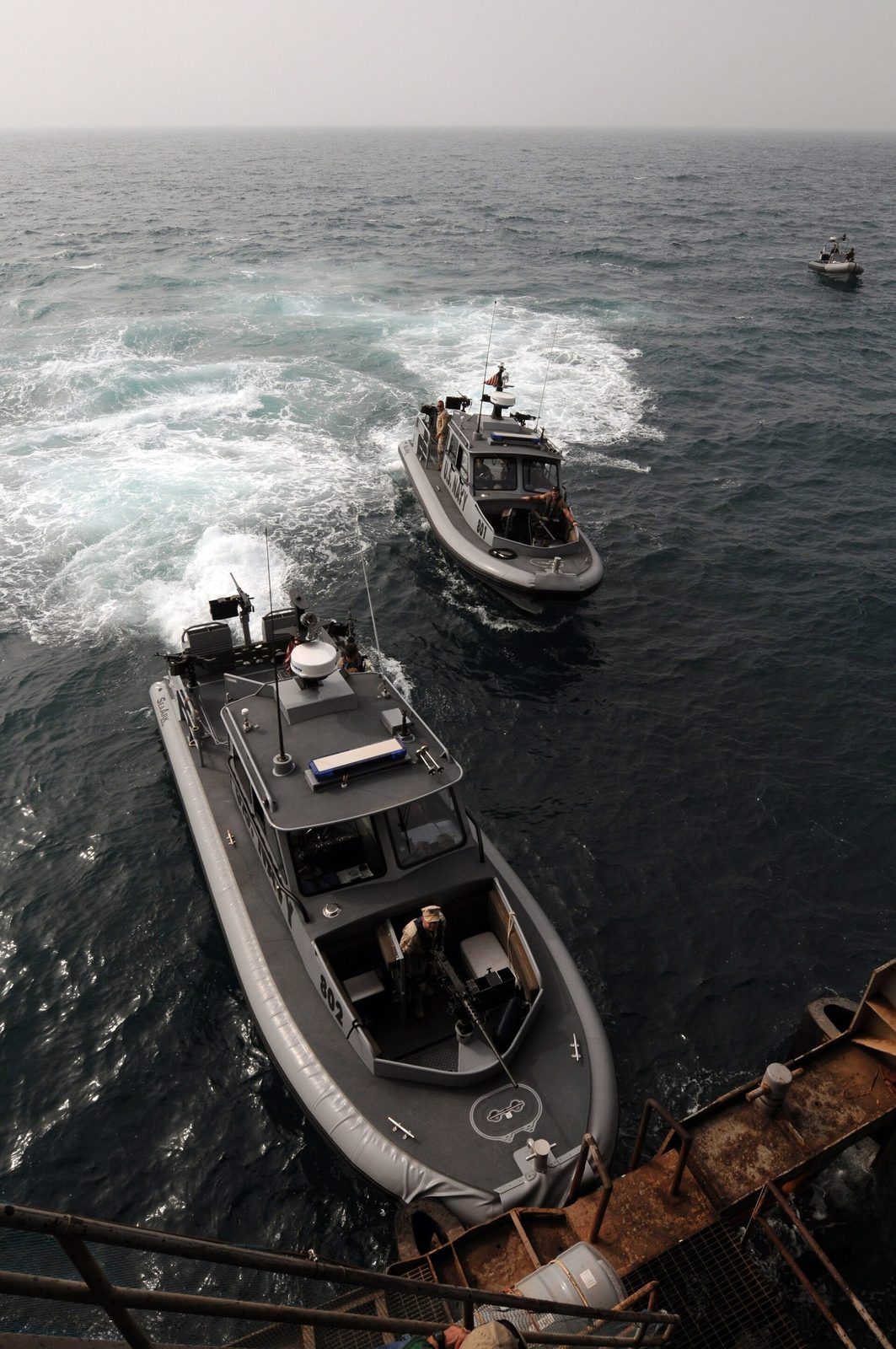 Two small patrol boats making wake beside oil terminal, viewed from above