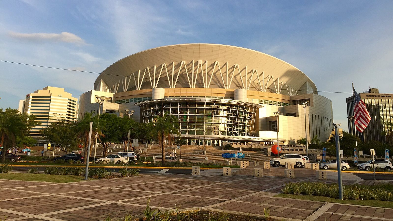 front view of large arena building, steps and parked cars visible