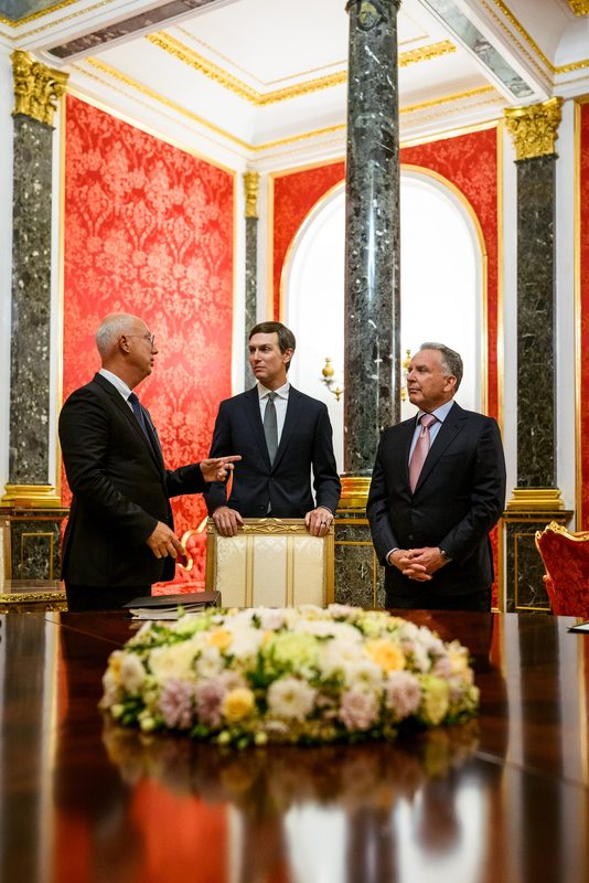 Three men standing in ornate red and gold room by a table