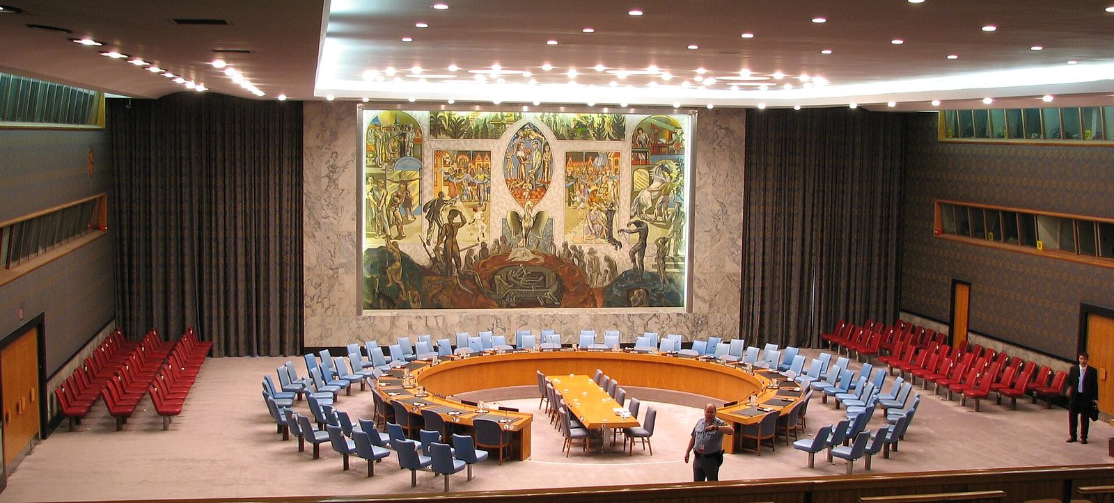 Empty circular council chamber, round table, large mural on wall (cropped)