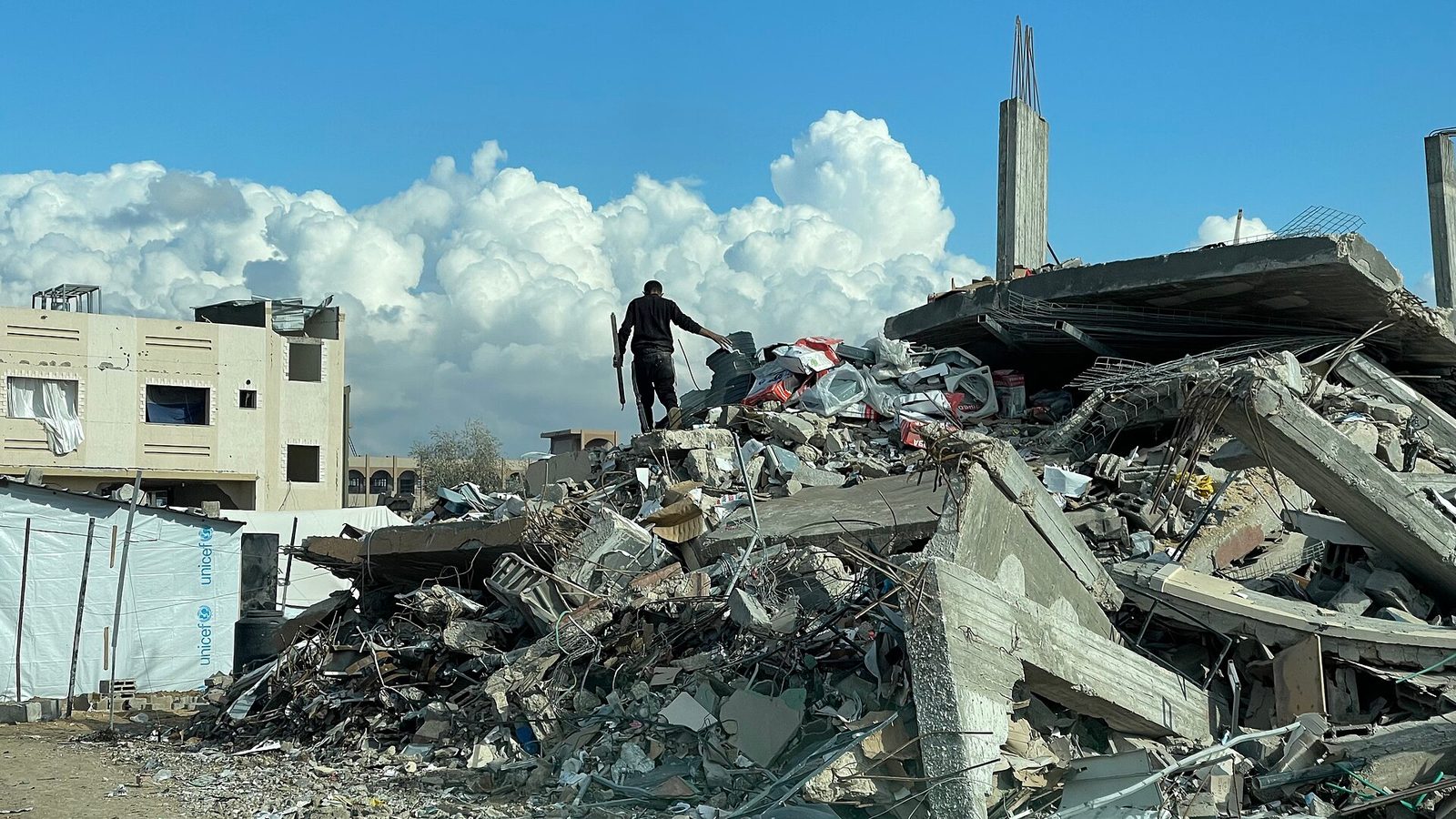 Man standing on pile of building rubble, sky behind