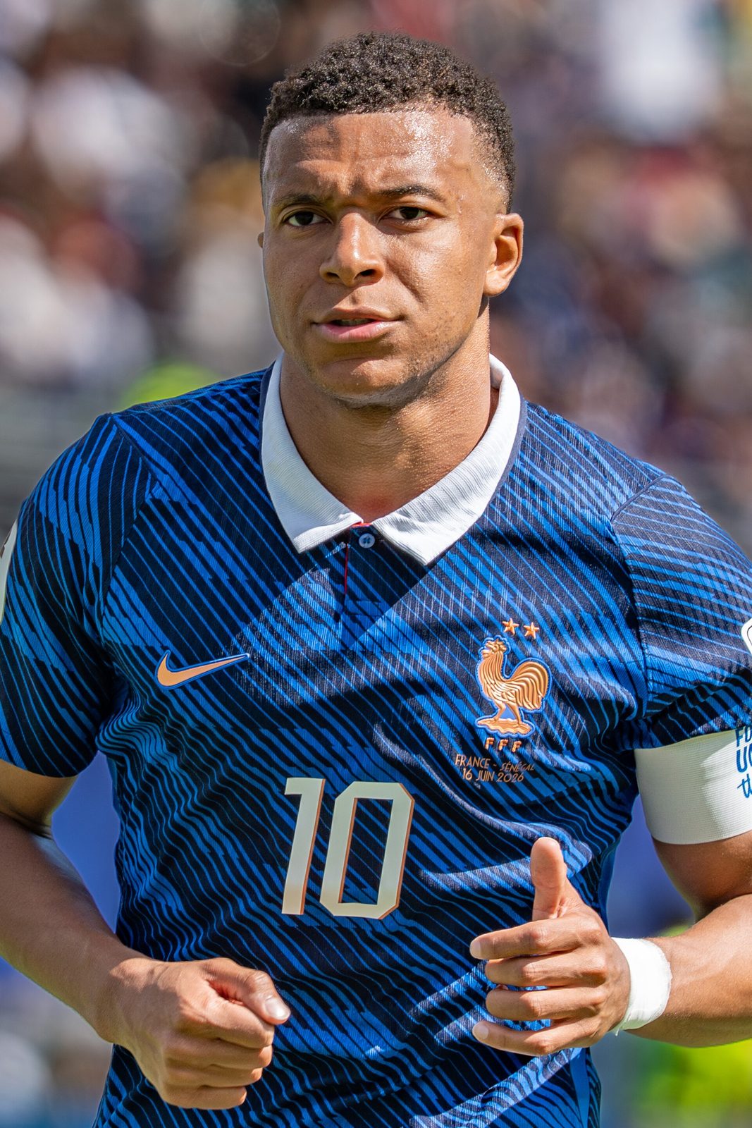 portrait of footballer in blue France jersey, blurred stadium crowd behind