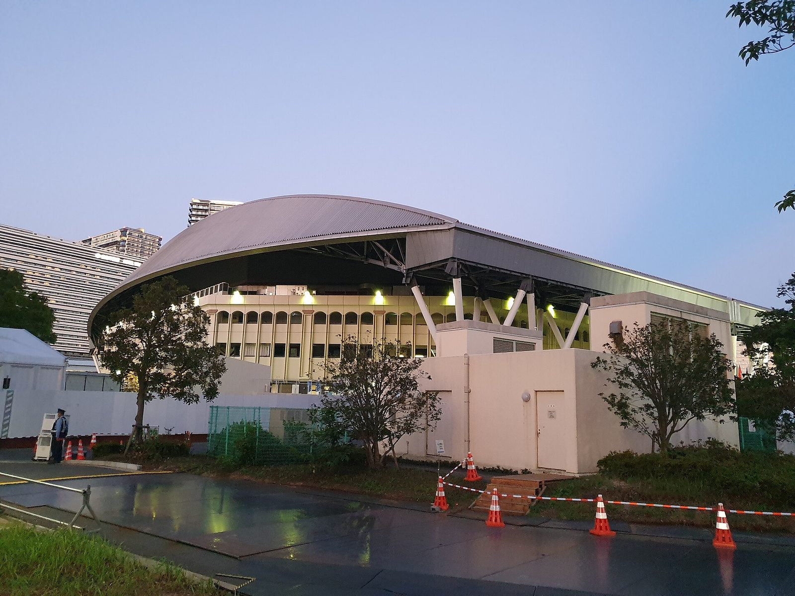 Side view of a domed sports arena at dusk, trees foreground, Ariake Coliseum