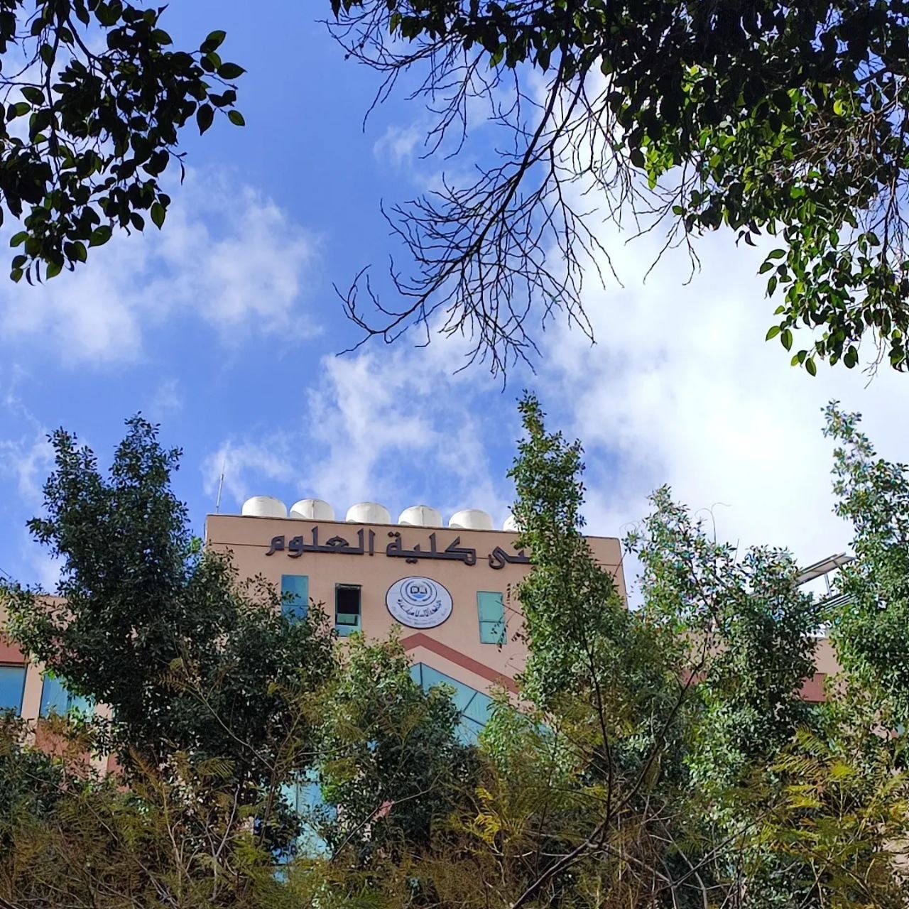University building façade with Arabic name visible above trees
