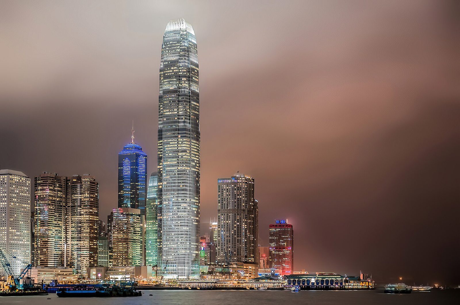 Tall illuminated skyscrapers at night under a brooding, stormy sky, Hong Kong